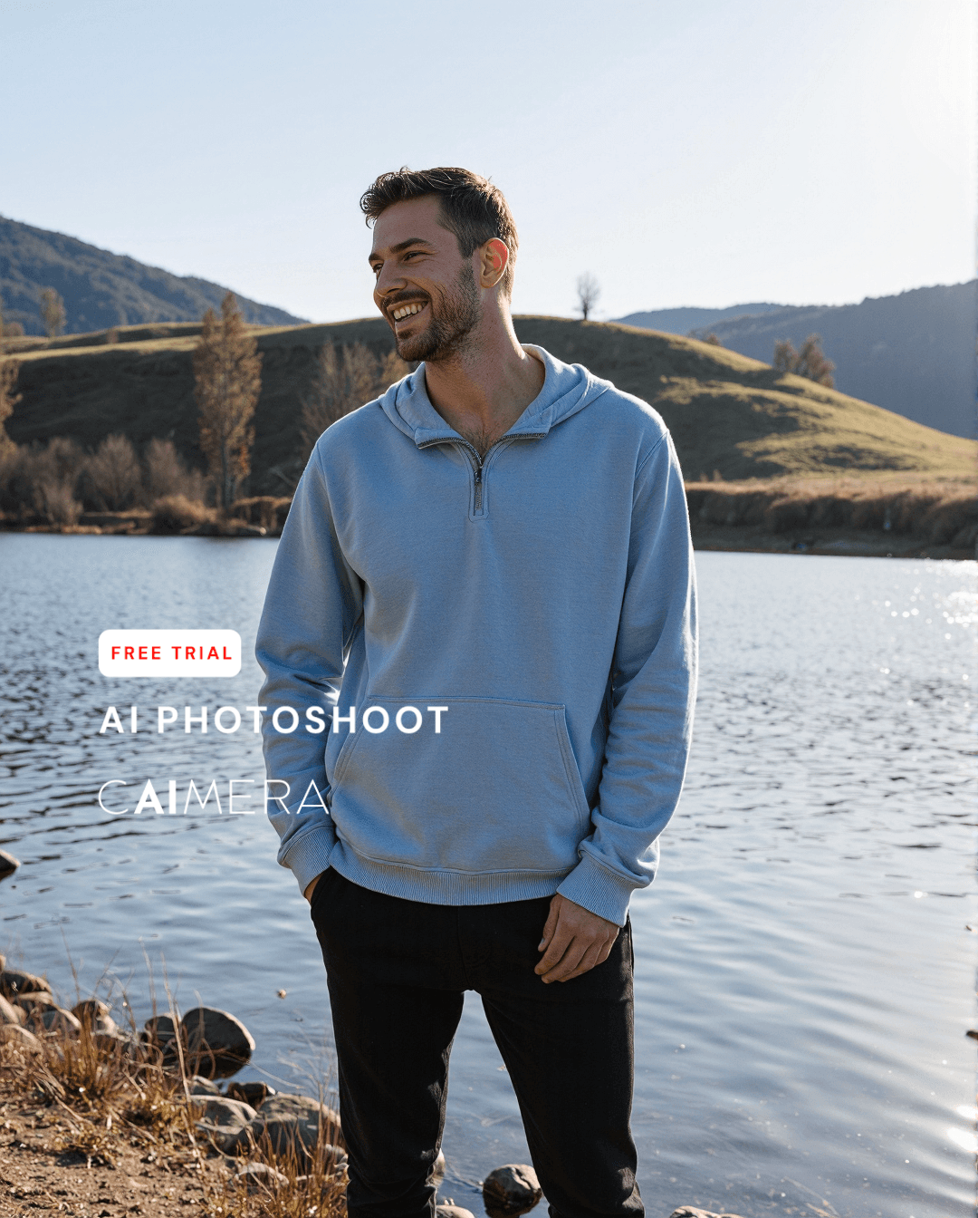 Person in light blue hoodie smiling by a lake with rolling hills in background, captured in warm natural sunlight