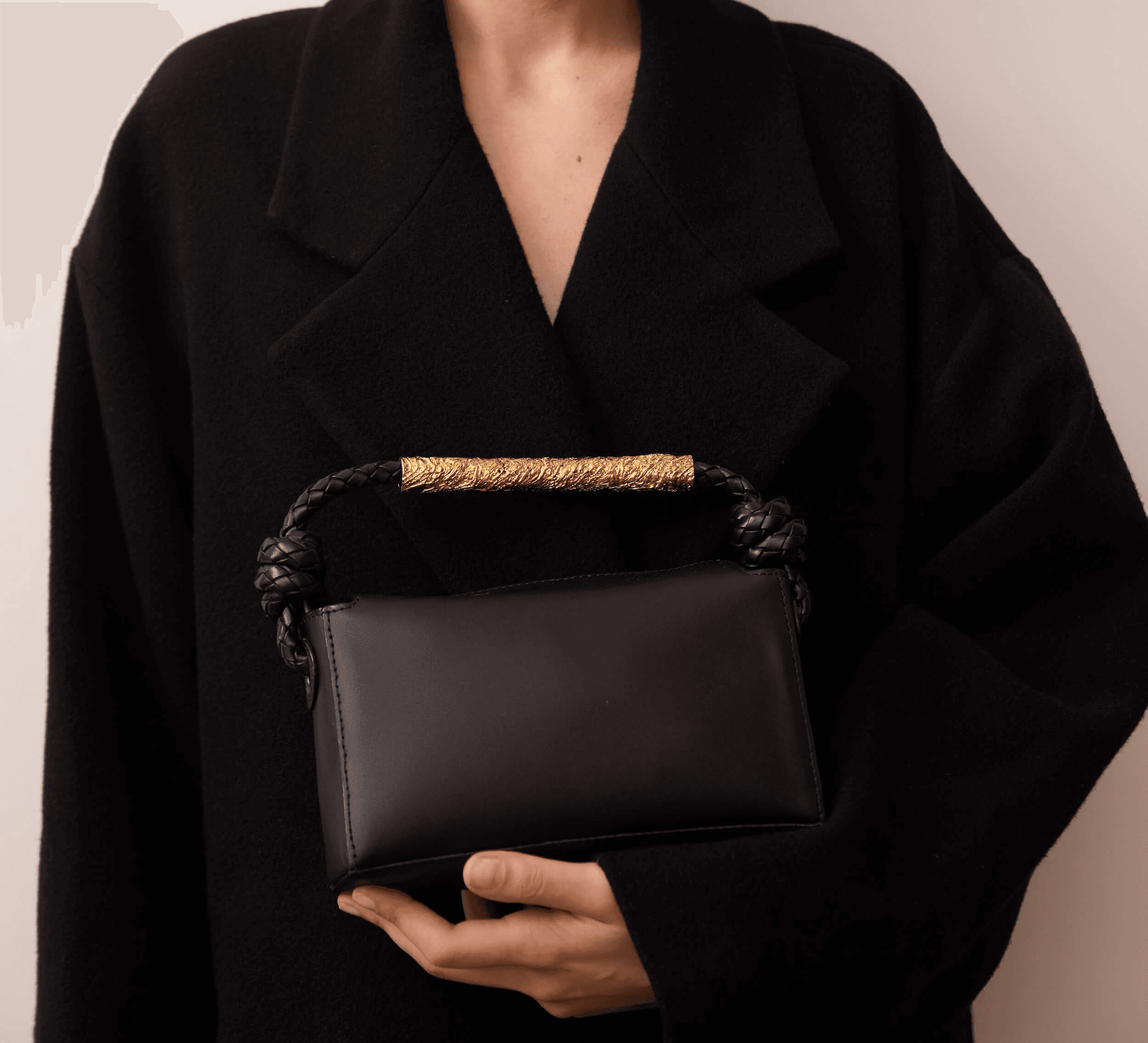Close-up of a woman wearing a chunky ribbed beige sweater, gently covering her mouth with the collar. She wears a matte black sculptural earring with gold hardware, and her eyes are softly closed in a calm, introspective pose.