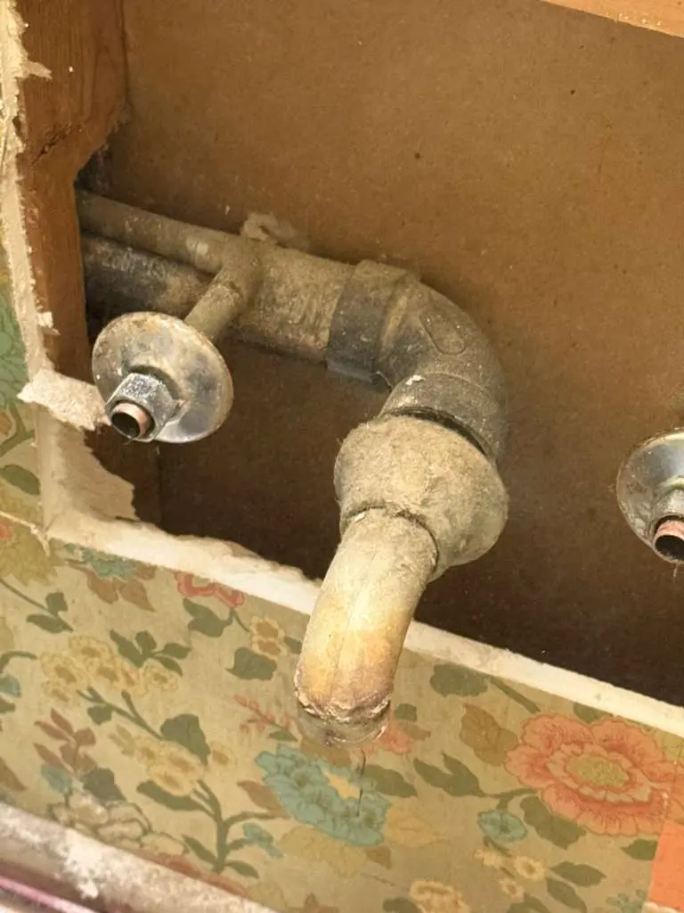 A heavily corroded indoor plumbing pipe exposed behind a wall cutout, evaluated for a professional water line repair.