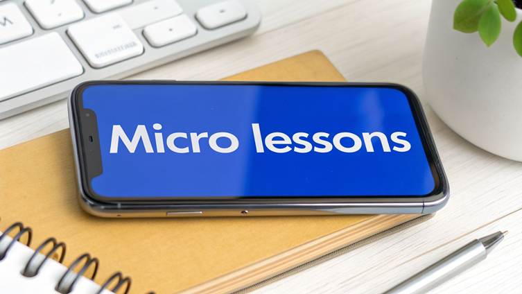 Smartphone displaying 'Micro lessons' on a blue screen, on a desk with a keyboard and notebook.