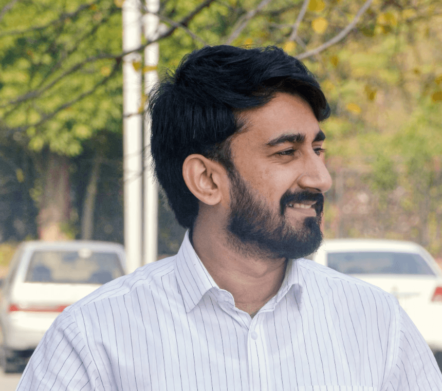 a young man wearing glasses standing in front of a mountain