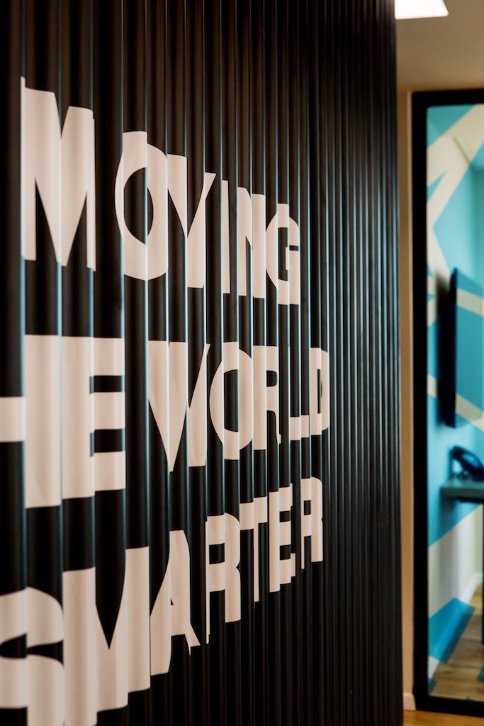 עיצוב משרדים מבוסס מיתוג: דלפק כניסה פיסולי בצורת הלוגו, המשלב צמחייה וניגודיות מול קיר האבן הטבעית