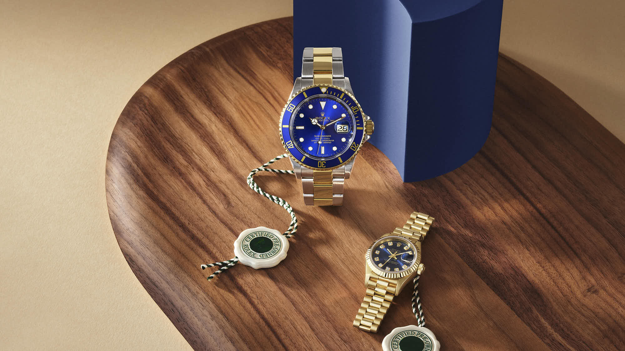 A stylish wooden tray presents two gold watches with blue dials