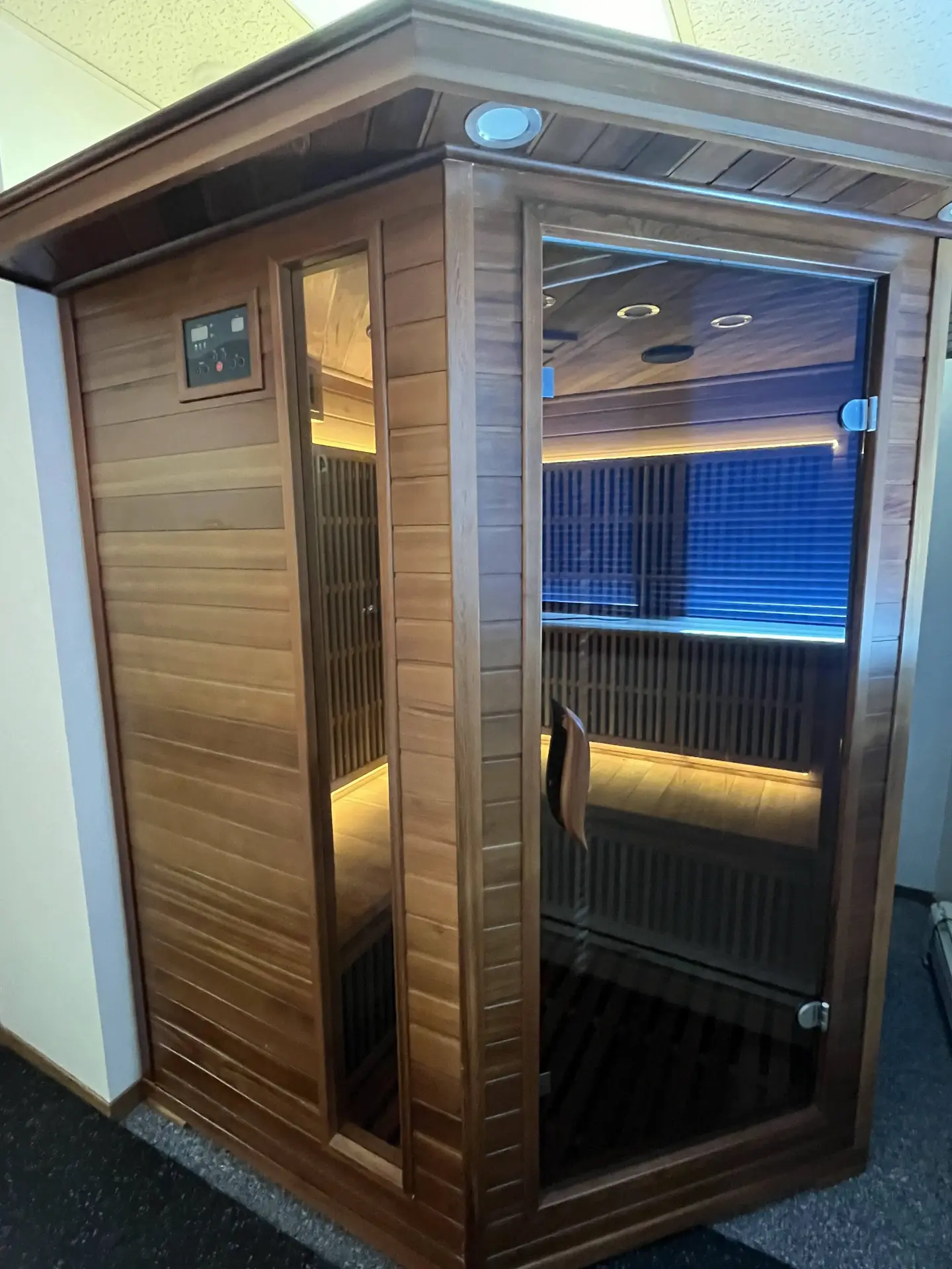 Wooden sauna cabin with a glass door and illuminated interior.