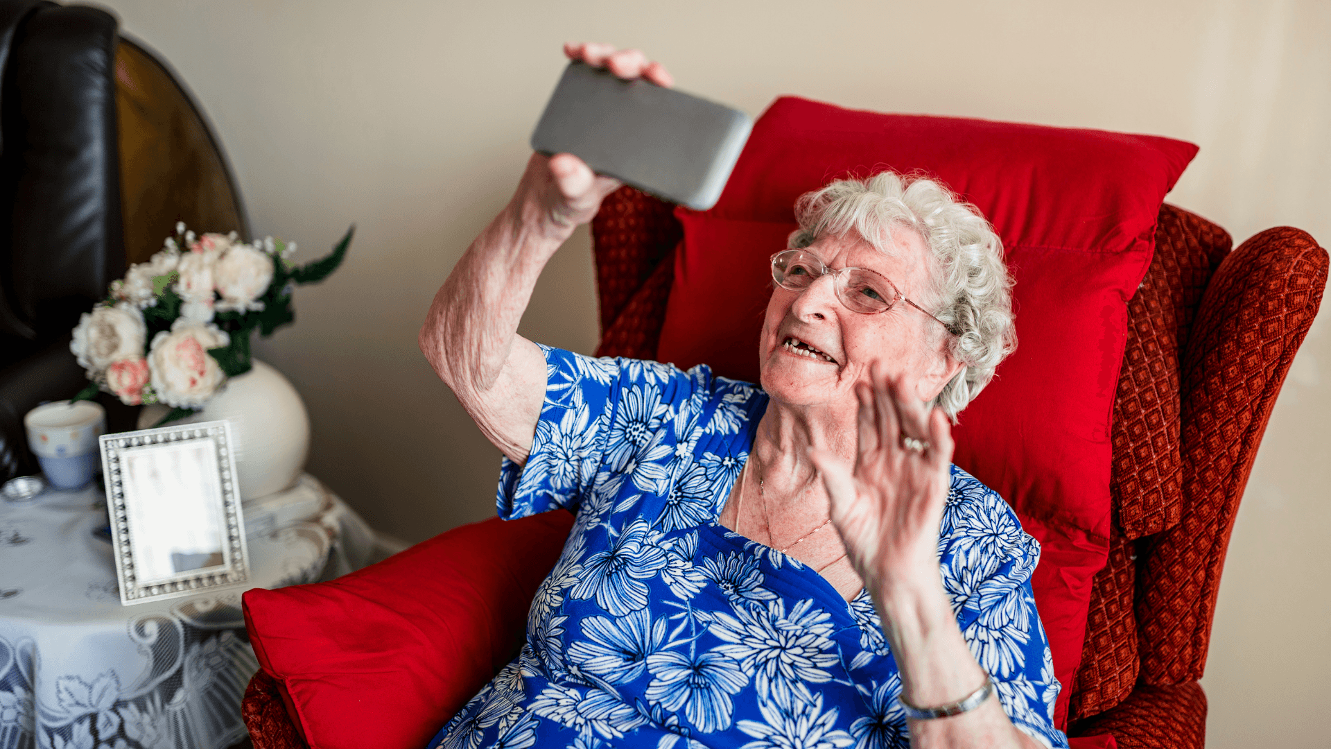 An older woman waving at someone she's video calling on a mobile phone