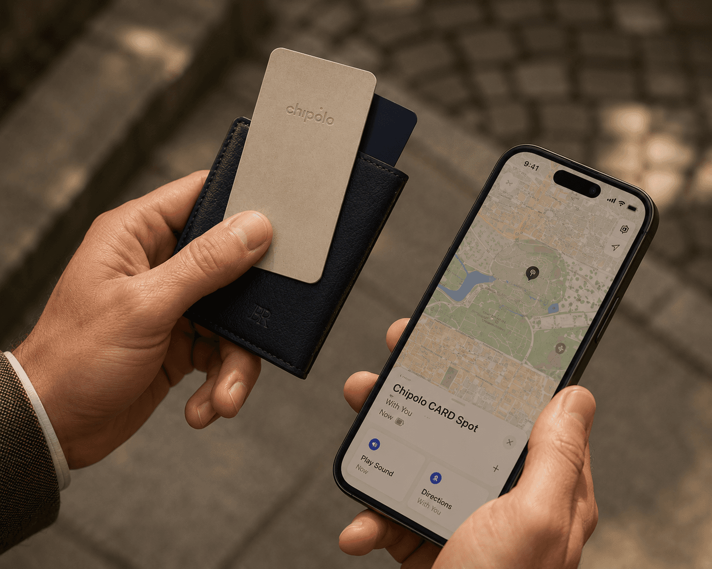 An outdoor close-up shot of a person holding a navy blue leather cardholder wallet in one hand and a smartphone in the other on a paved street. A beige Chipolo CARD Spot item tracker card is partially slid out of the wallet pocket. The smartphone screen displays the Apple Find My application tracking interface for the Chipolo card over a city map layout.