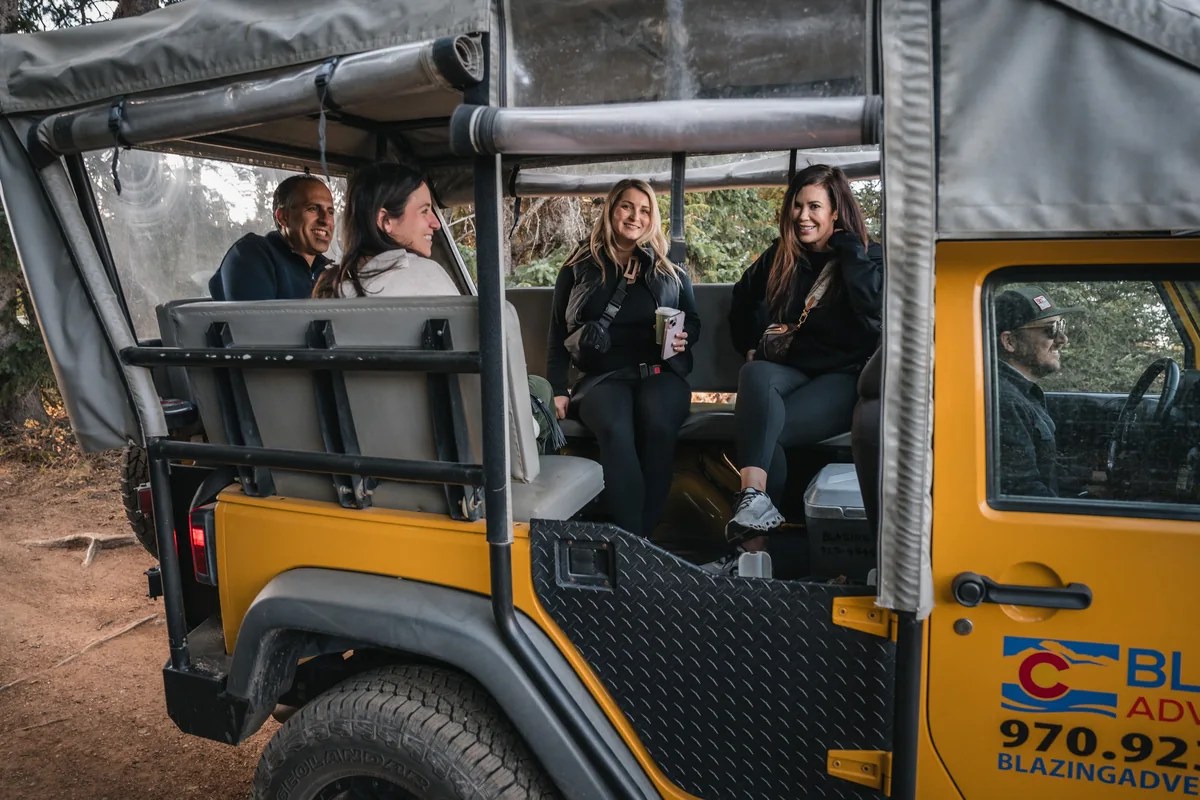 Retreat guests smile from the open rear seats of a yellow Jeep.