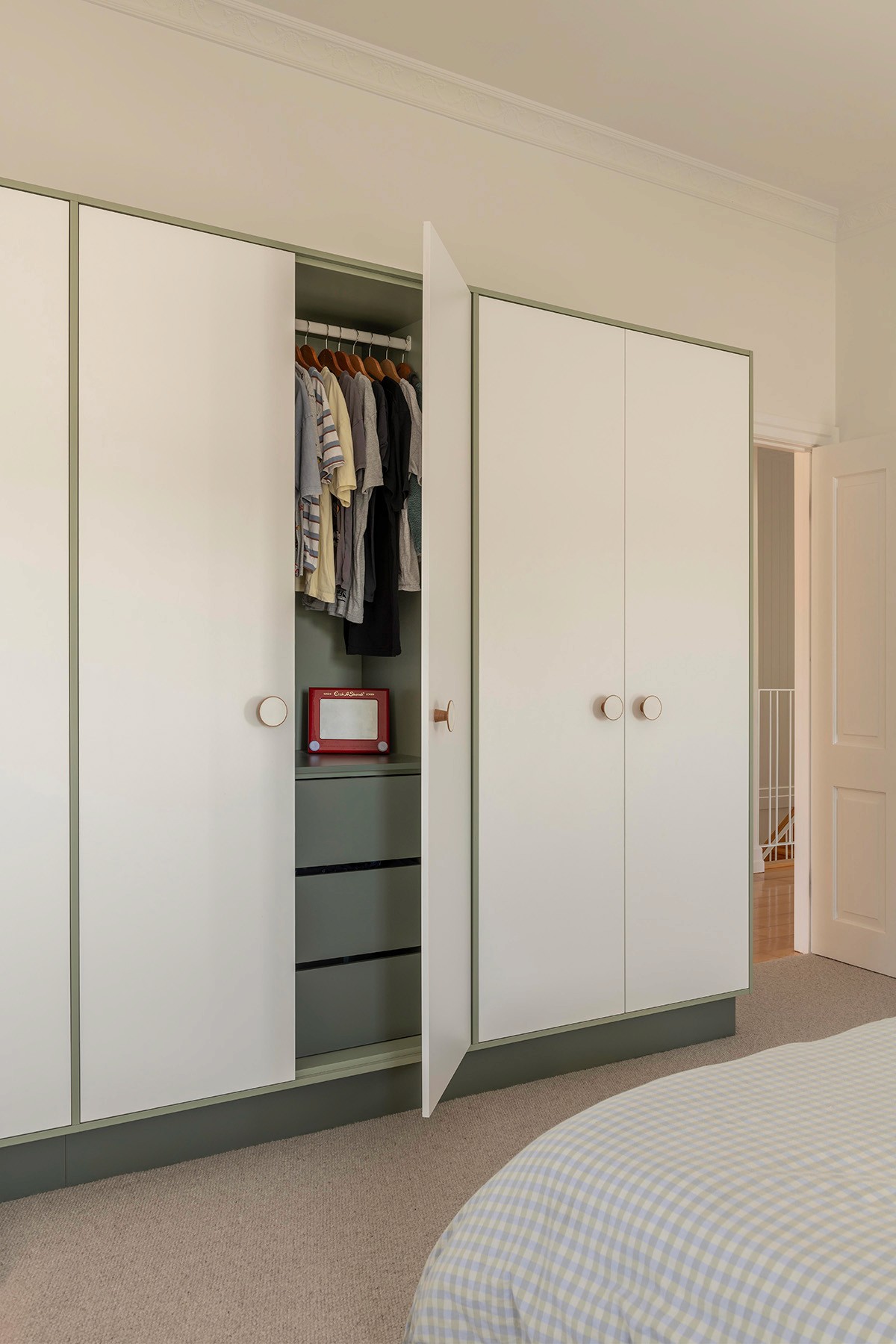 Built-in bedroom wardrobes with sliding doors, muted green interior, and integrated hanging and drawer storage.