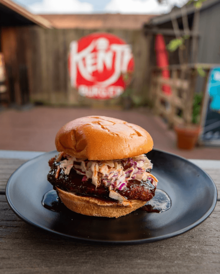 A plate of five savory soft-shell tacos, generously filled with seasoned meat, cilantro, and shredded cheese, presented in a dimly lit, atmospheric setting with a lit candle and a copper vessel in the background.