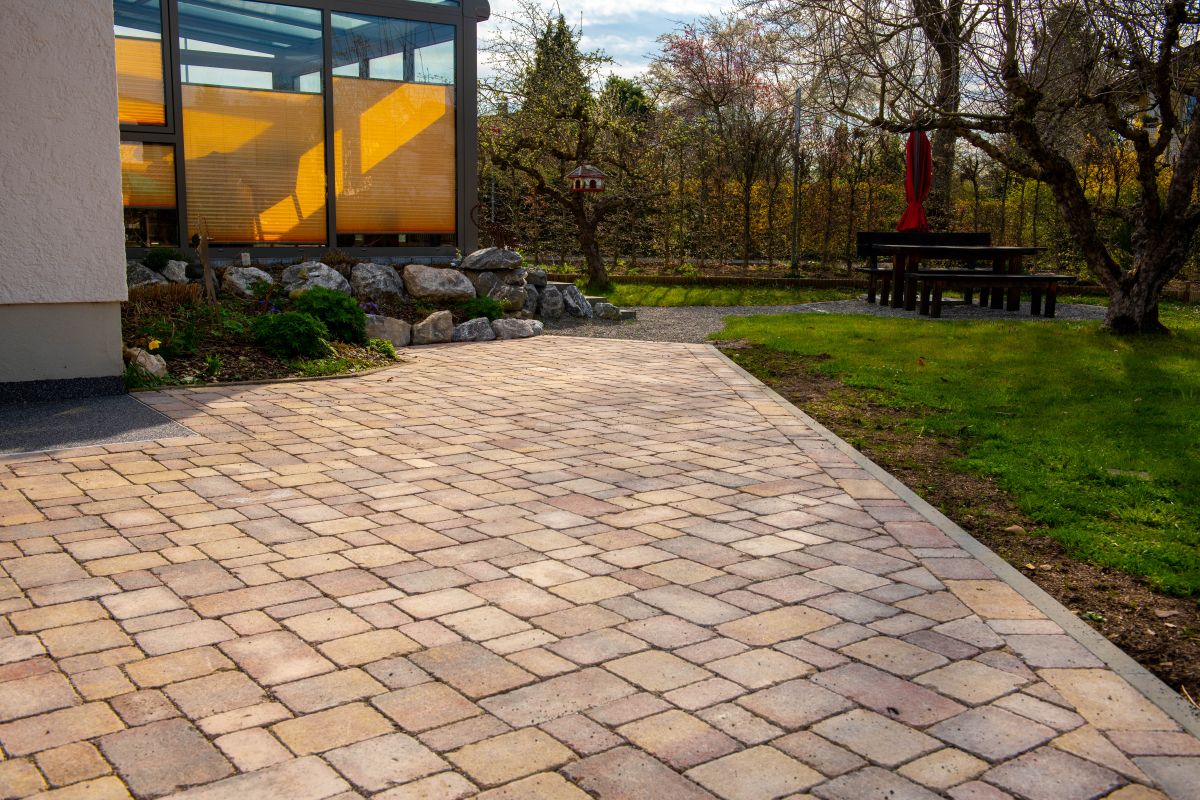 Fachgerecht verlegte Terrasse mit buntem Pflasterstein, angrenzender Naturstein-Böschung und Blick in einen gepflegten Garten, Gartengestaltung Klingenstein.