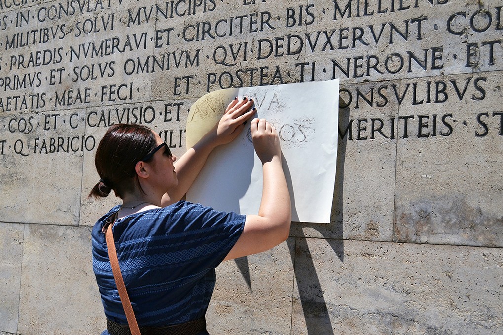 student shaving the graphite pen to a paper and put over an engraved text on the wall