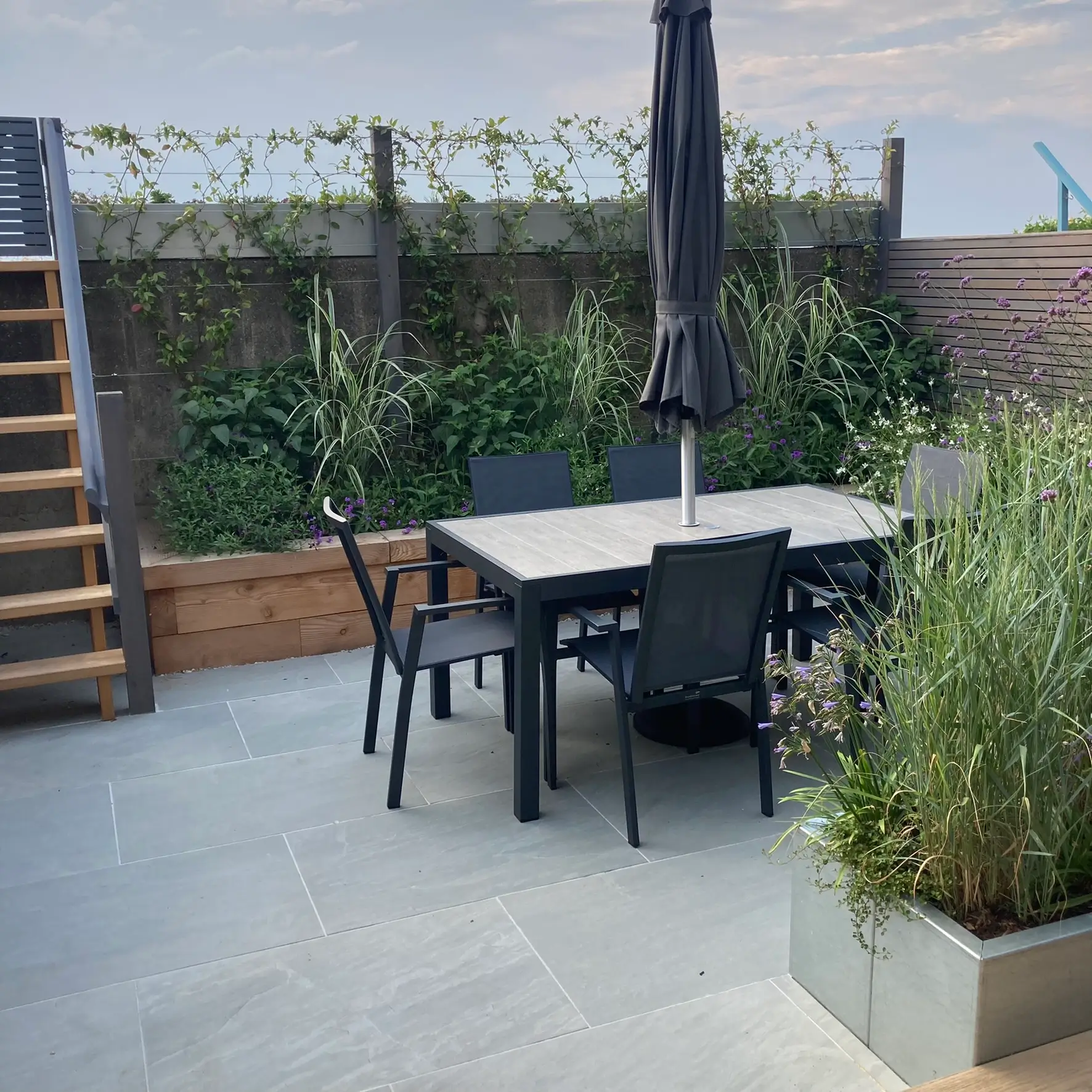 A modern outdoor dining area featuring a table, chairs, and greenery in a serene setting.