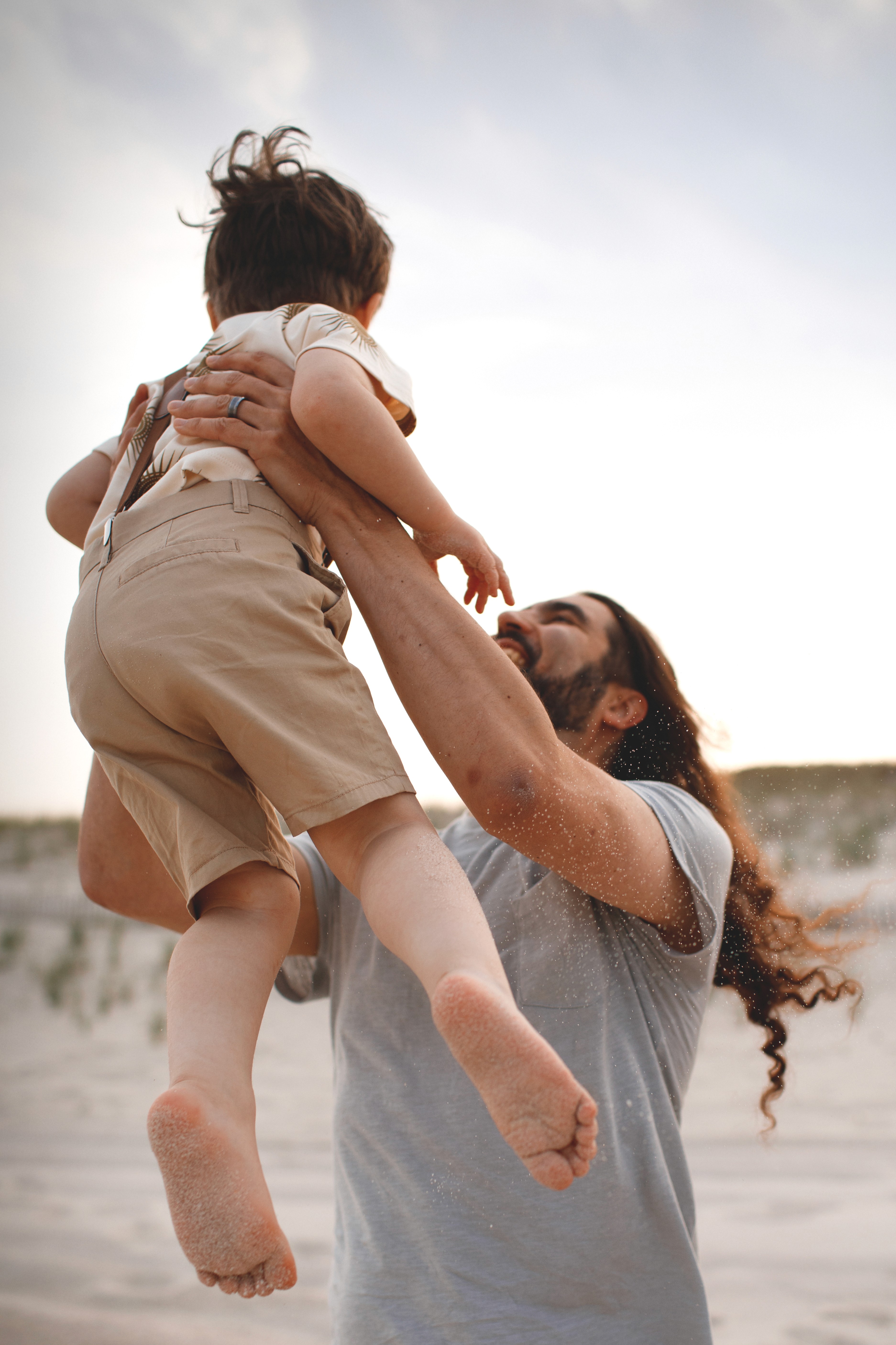 Parents lifting and spinning their child during a joyful beach family session.