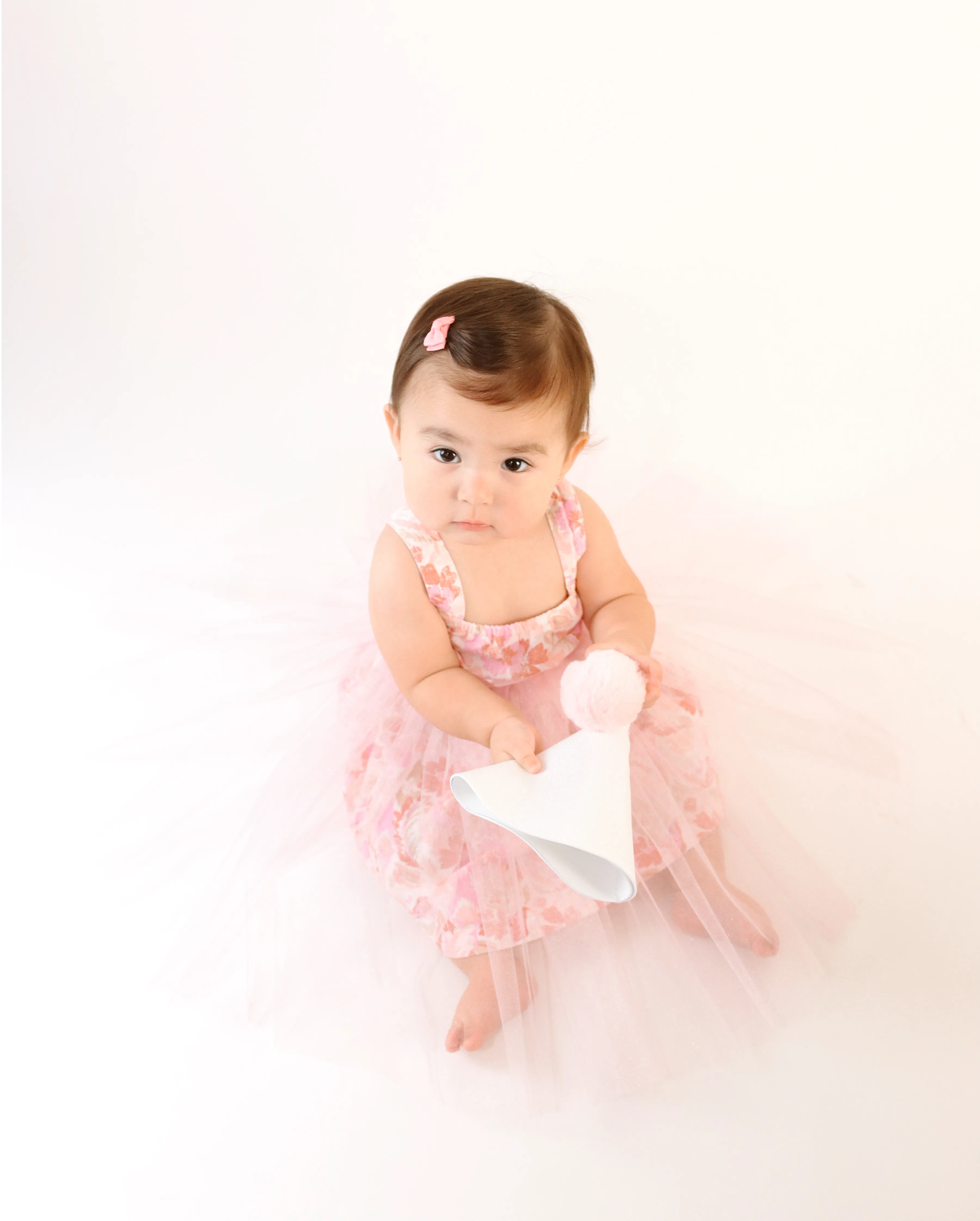 Bebé con tutú rosa sosteniendo un gorrito de fiesta blanco