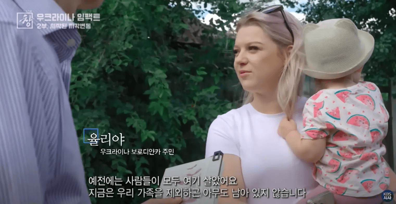 우크라이나 보로디얀카 주민 율리야가 아이를 안고 인터뷰하는 모습. 자막: "예전에는 사람들이 모두 여기 살았어요. 지금은 우리 가족을 제외하곤 아무도 남아 있지 않습니다"