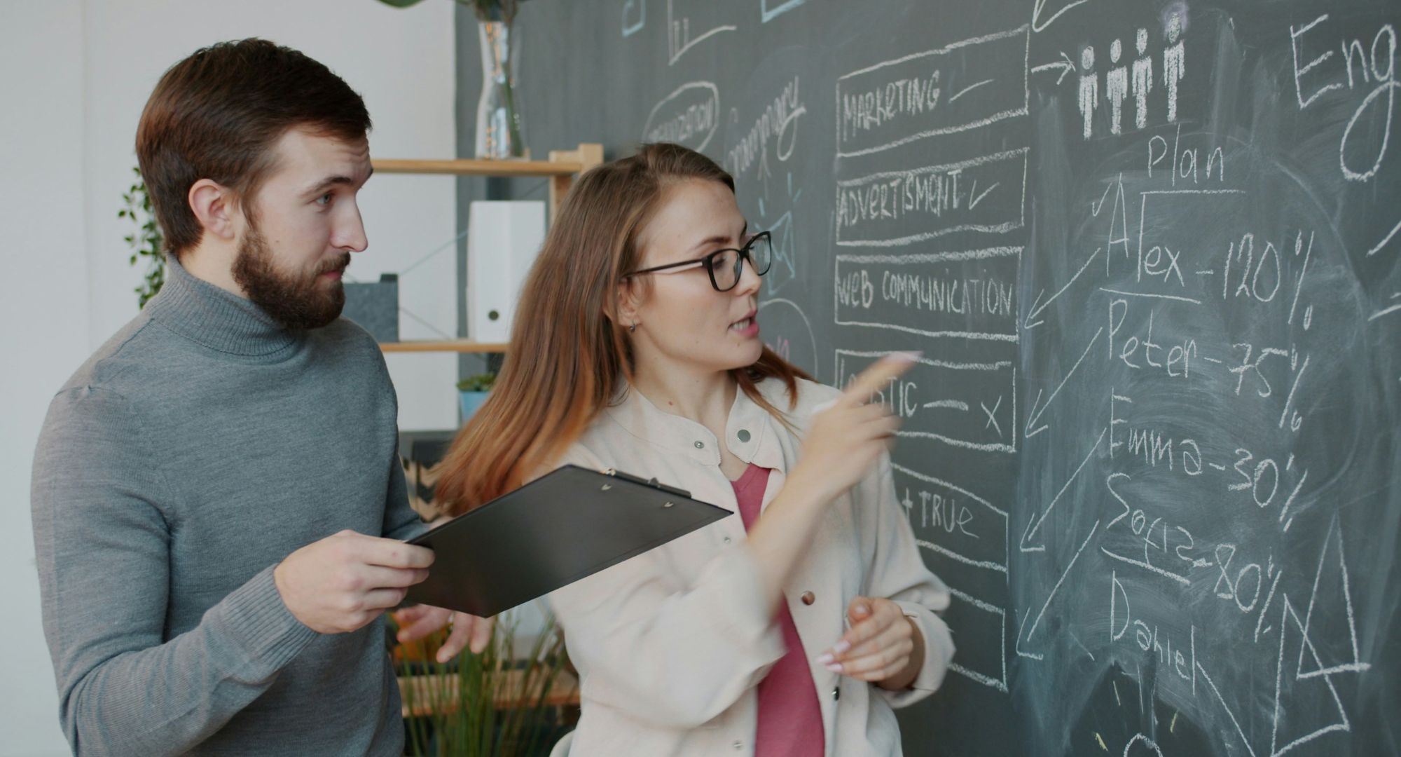 homem e mulher analisando porcentagens em quadro negro