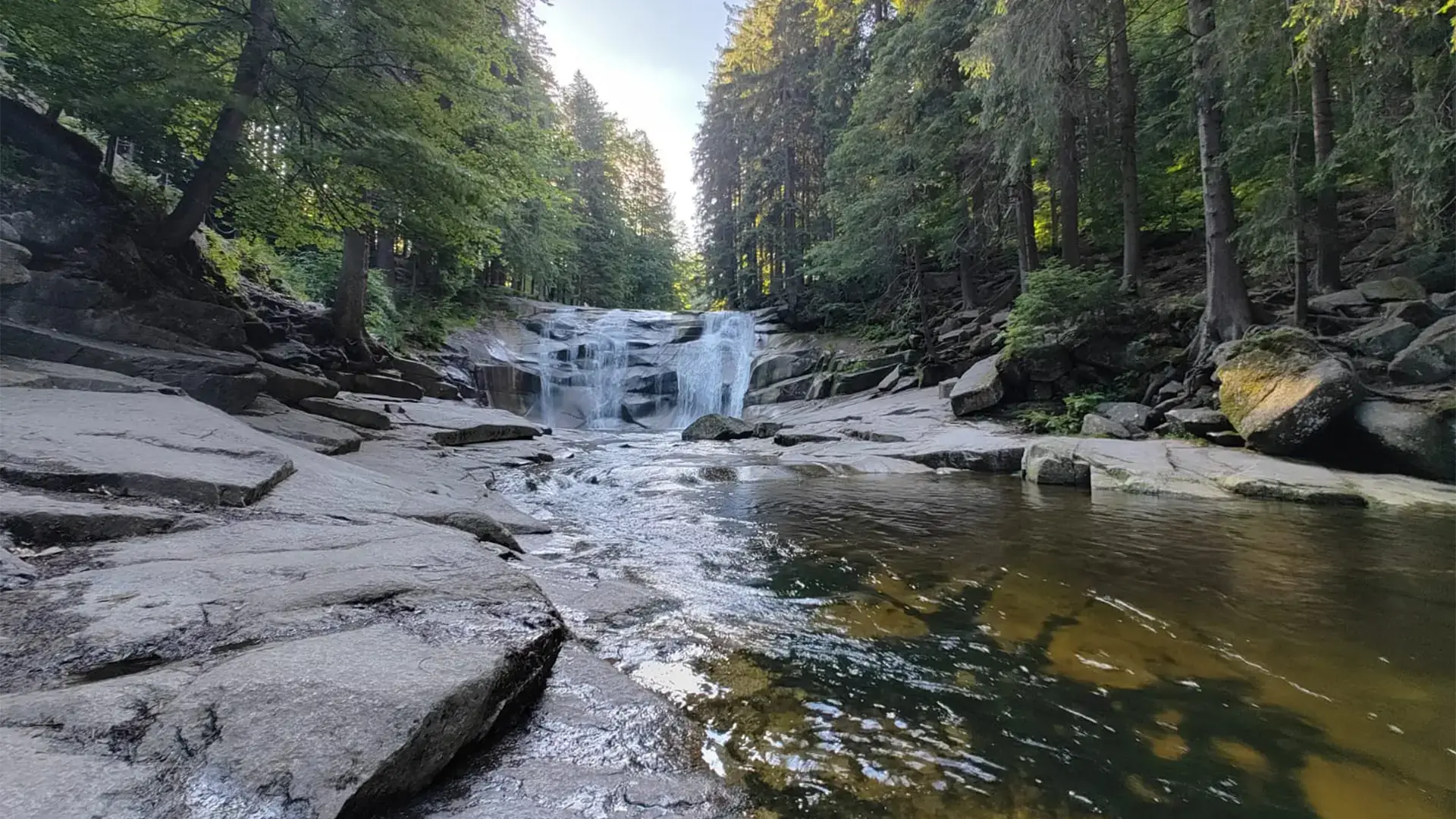Horský potok tekoucí přes kameny v lese. Detailní pohled na vodu, která je hlavním tématem dokumentu.