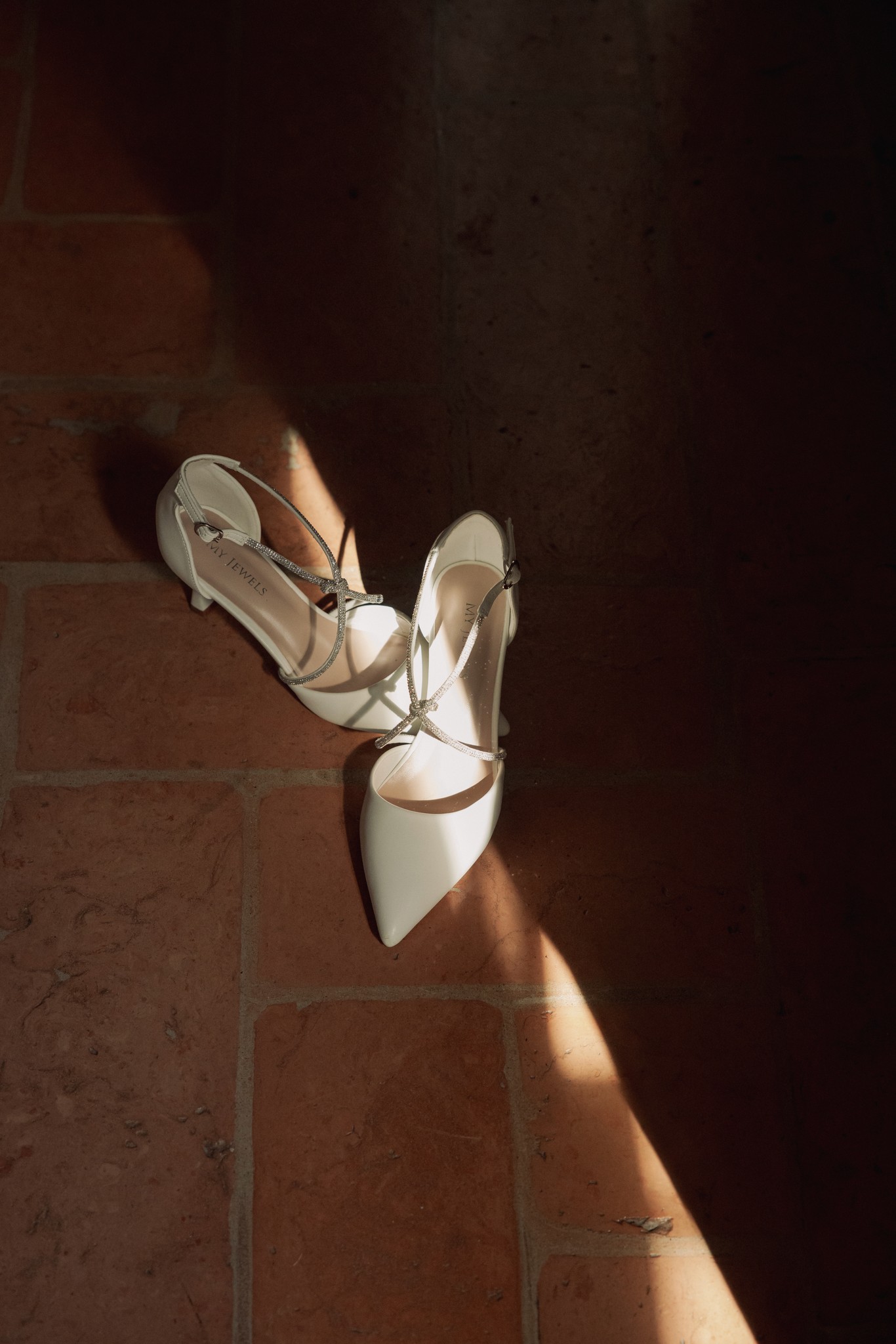 Scarpe da sposa bianche con dettagli dorati in luce naturale, su pavimento in cotto a Villa Negri
