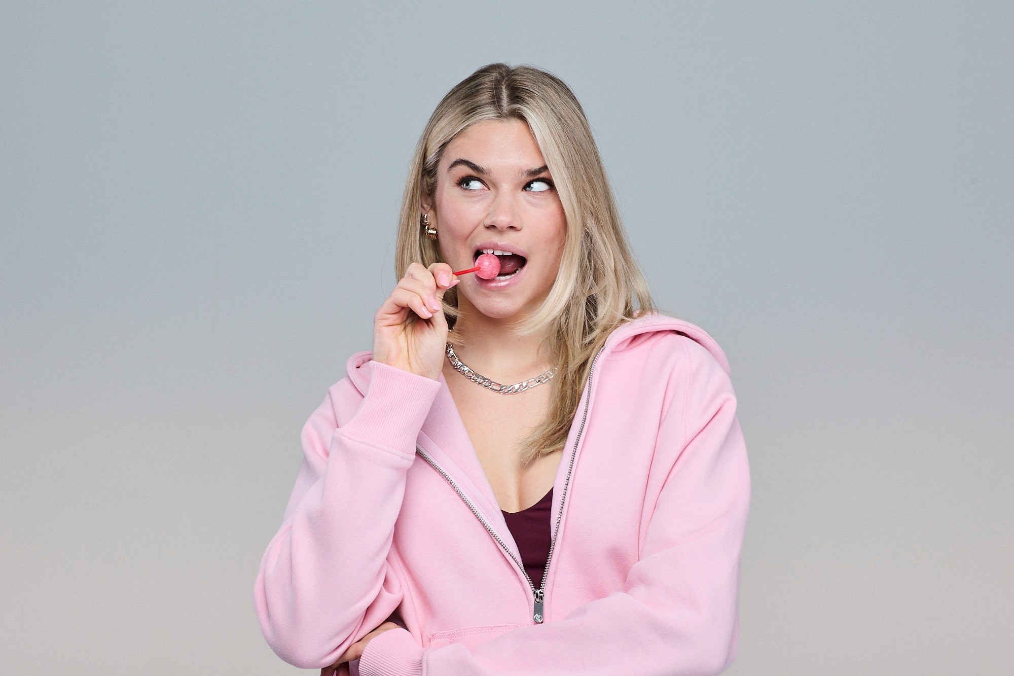 Woman wearing Sunday Superior pink zip hoodie with a lollypop in her hand