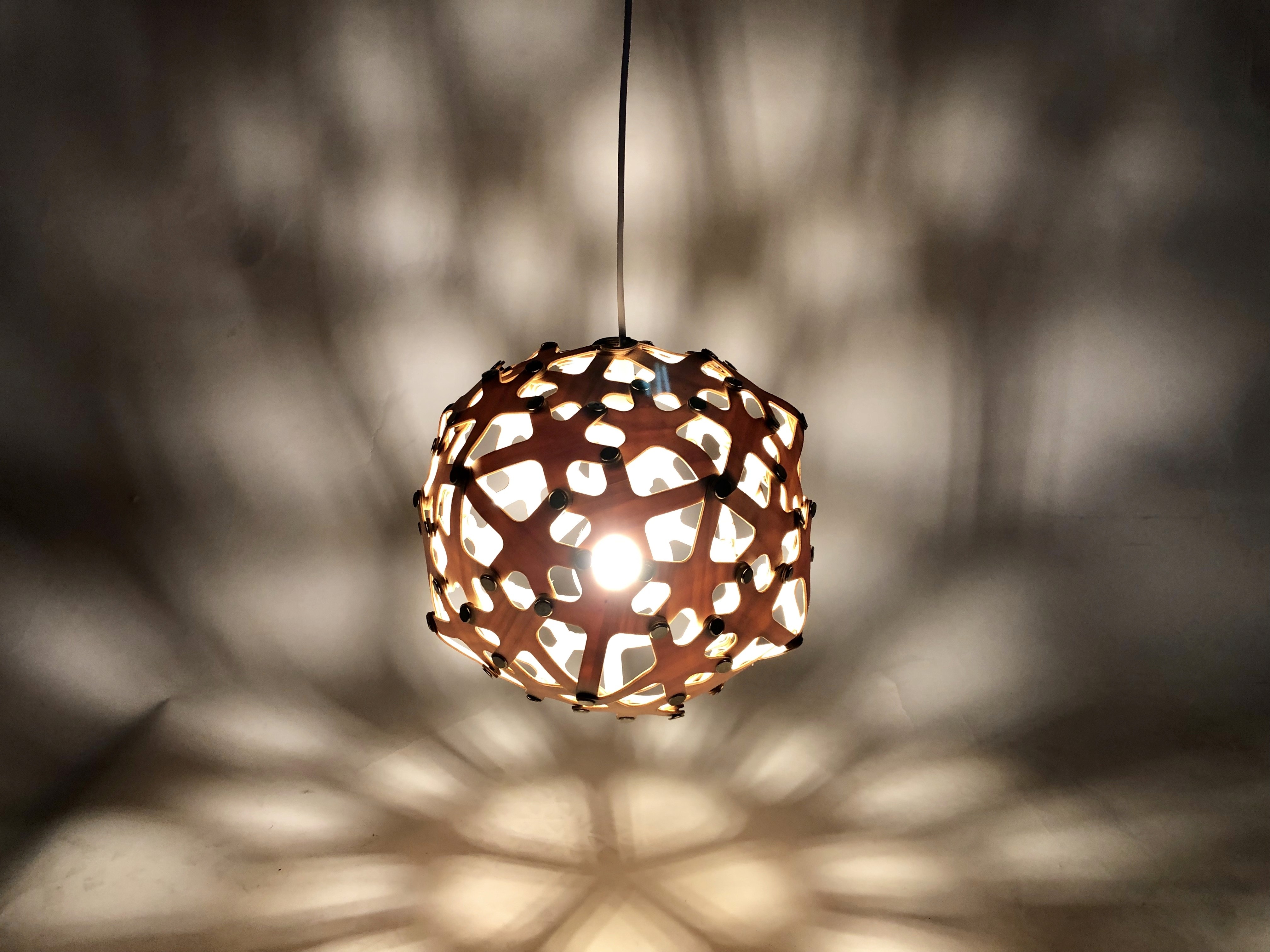 A laser-cut lighting prototype assembled from repeated wooden components. Identical shapes were cut from wood sheets and connected using a standardized screw system.