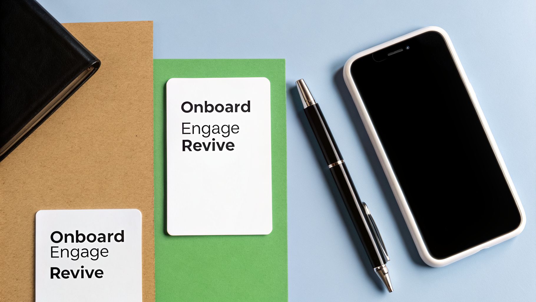 Flat lay showing two cards with 'Onboard Engage Revive' text, a smartphone, pen, and notebook.