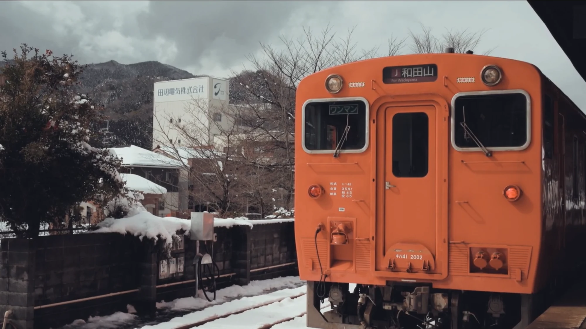 An orange two-car local train standing at a snow-covered platform on the Kinosaki line.