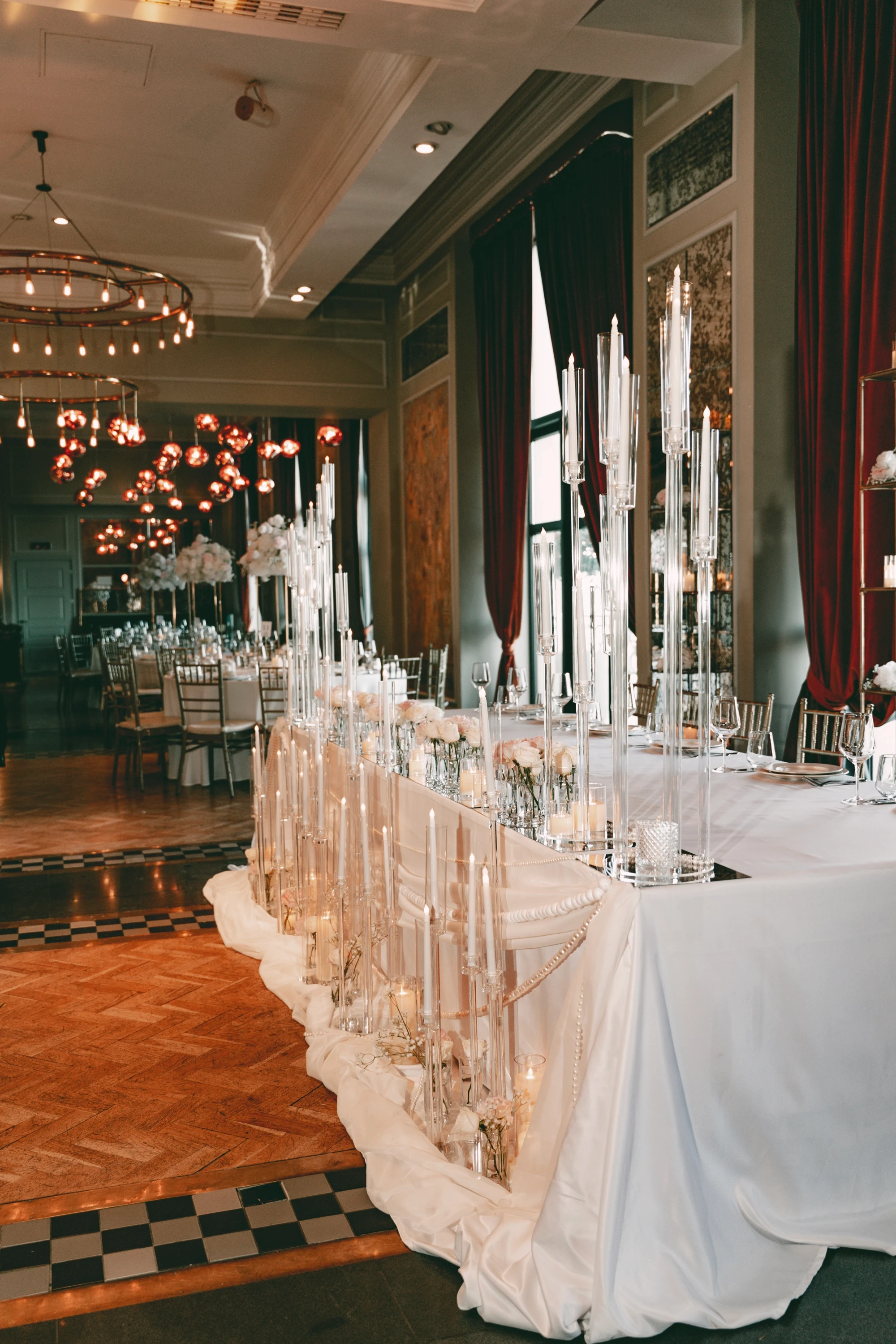 ძვირადღირებული ქორწილის საპატიო მაგიდის დეკორი სანთლებით, მარგალიტის დეტალებითა და ღია ვარდისფერი ყვავილებით ელეგანტურ დარბაზში