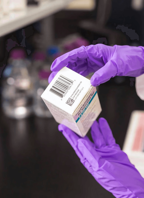 Close-up of a scientist wearing gloves inspecting medication packaging in a laboratory.