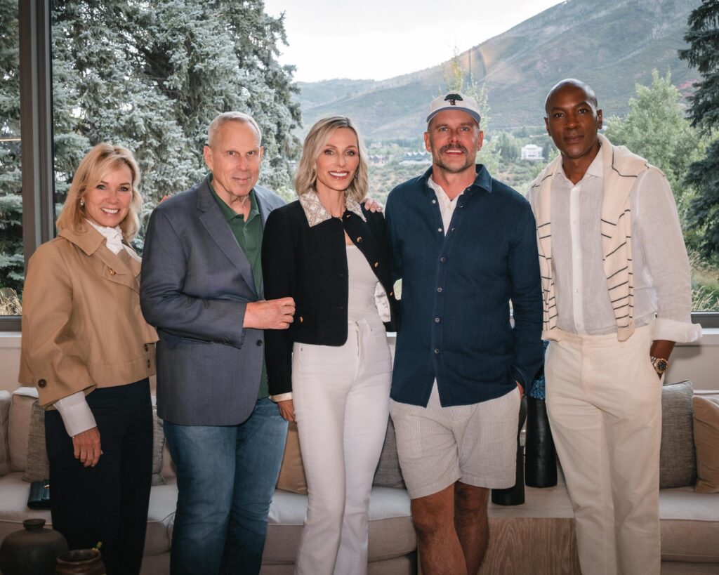 Five guests posing together in front of large windows overlooking wooded mountain slopes