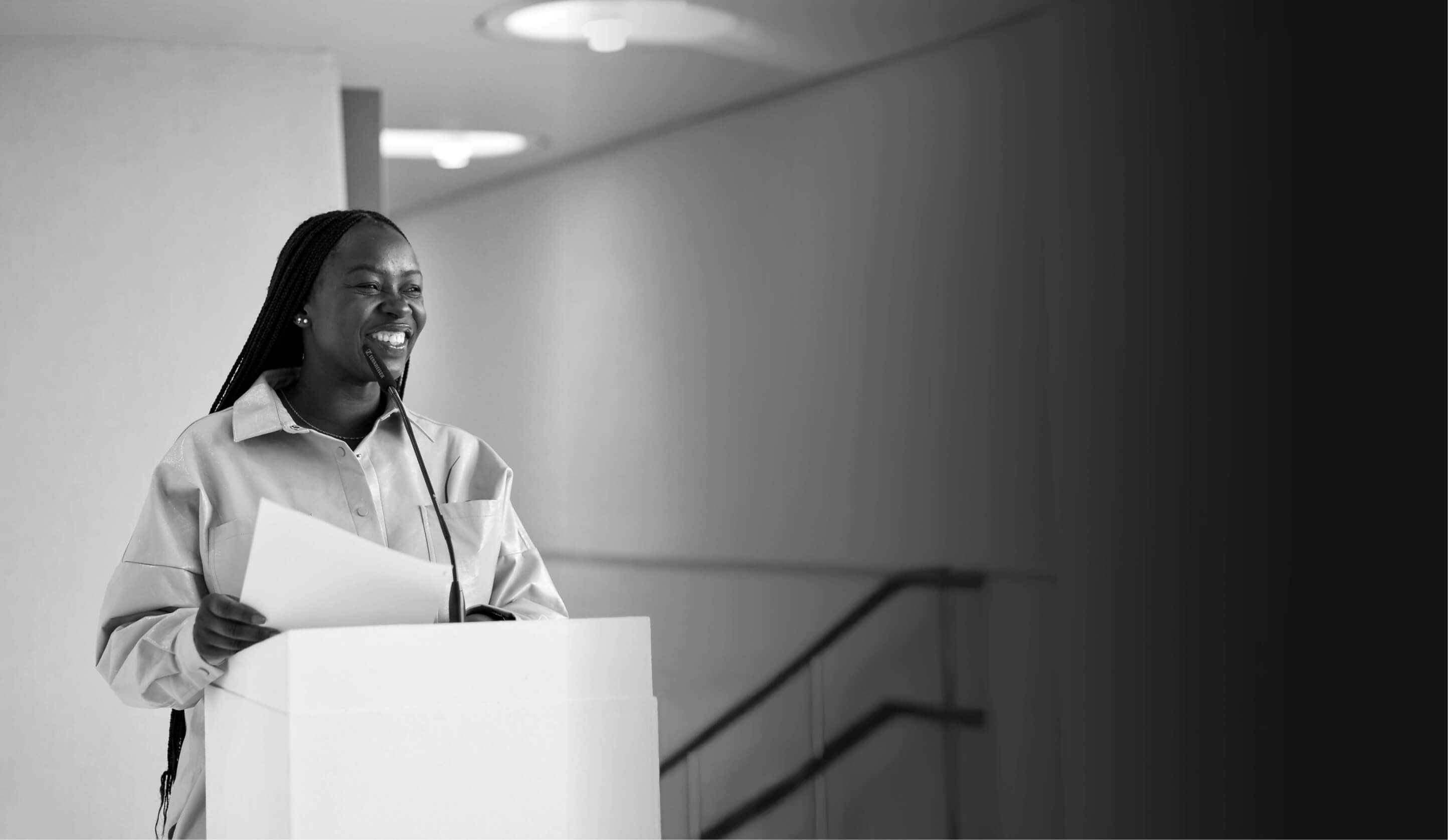Mary smiling while standing on a stage, giving a speech to an audience.