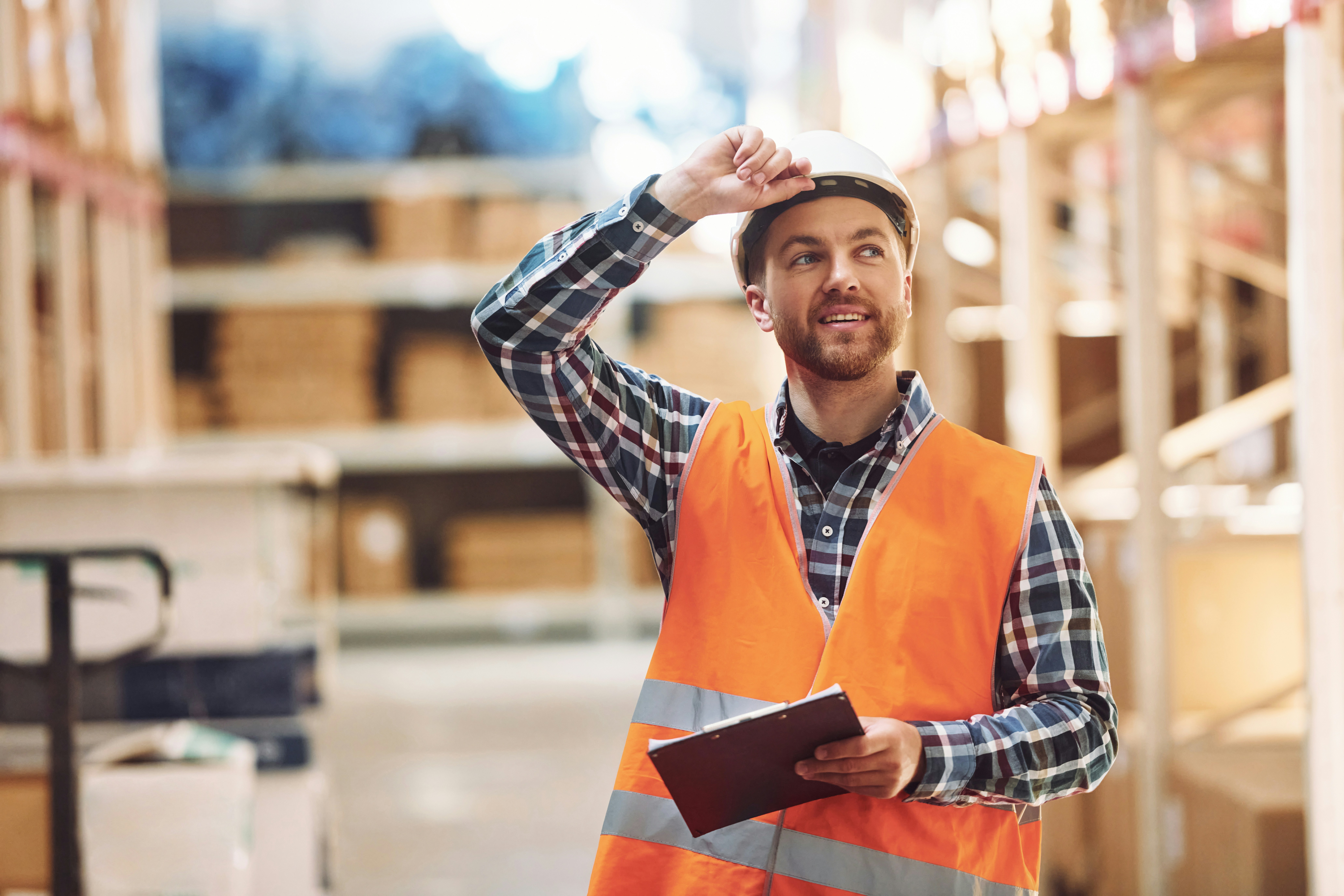 warehouse worker with clipboard holds his helmet