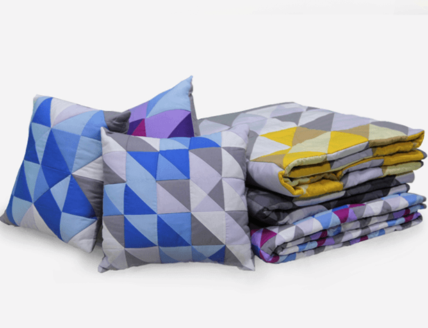 A close-up view of a quilt featuring a geometric pattern of triangles in yellow, gray, and off-white, designed with a repeating symmetrical layout and slight wrinkles, draped elegantly.