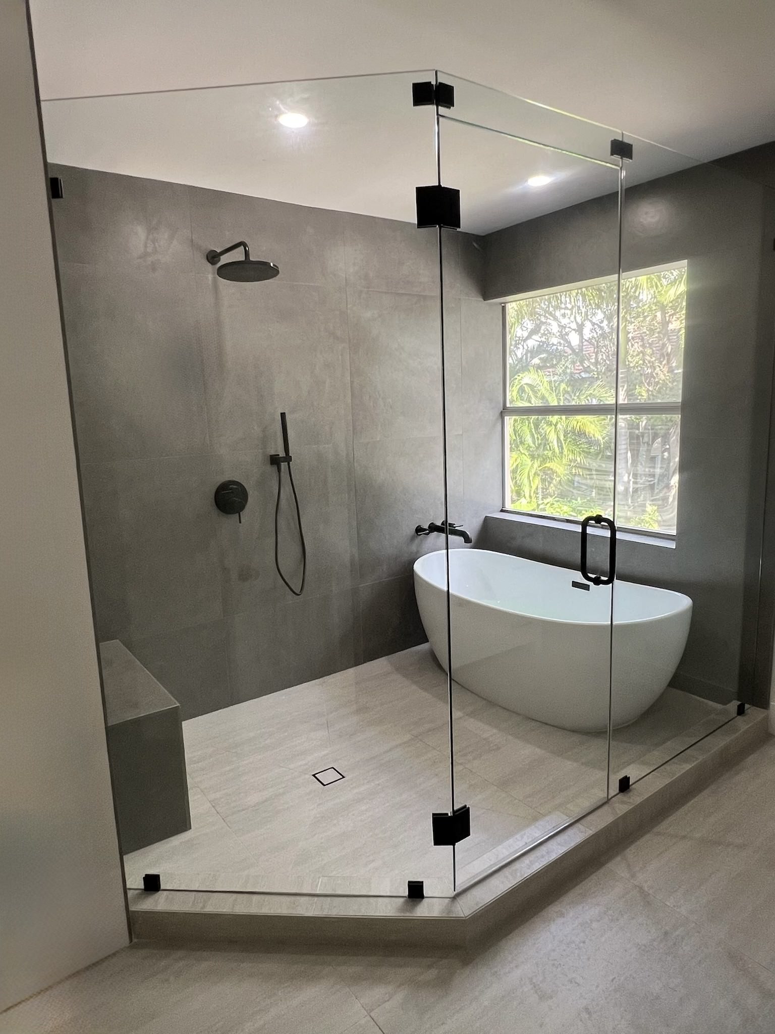 Modern bathroom featuring a glass shower, freestanding tub, and large window with natural light.