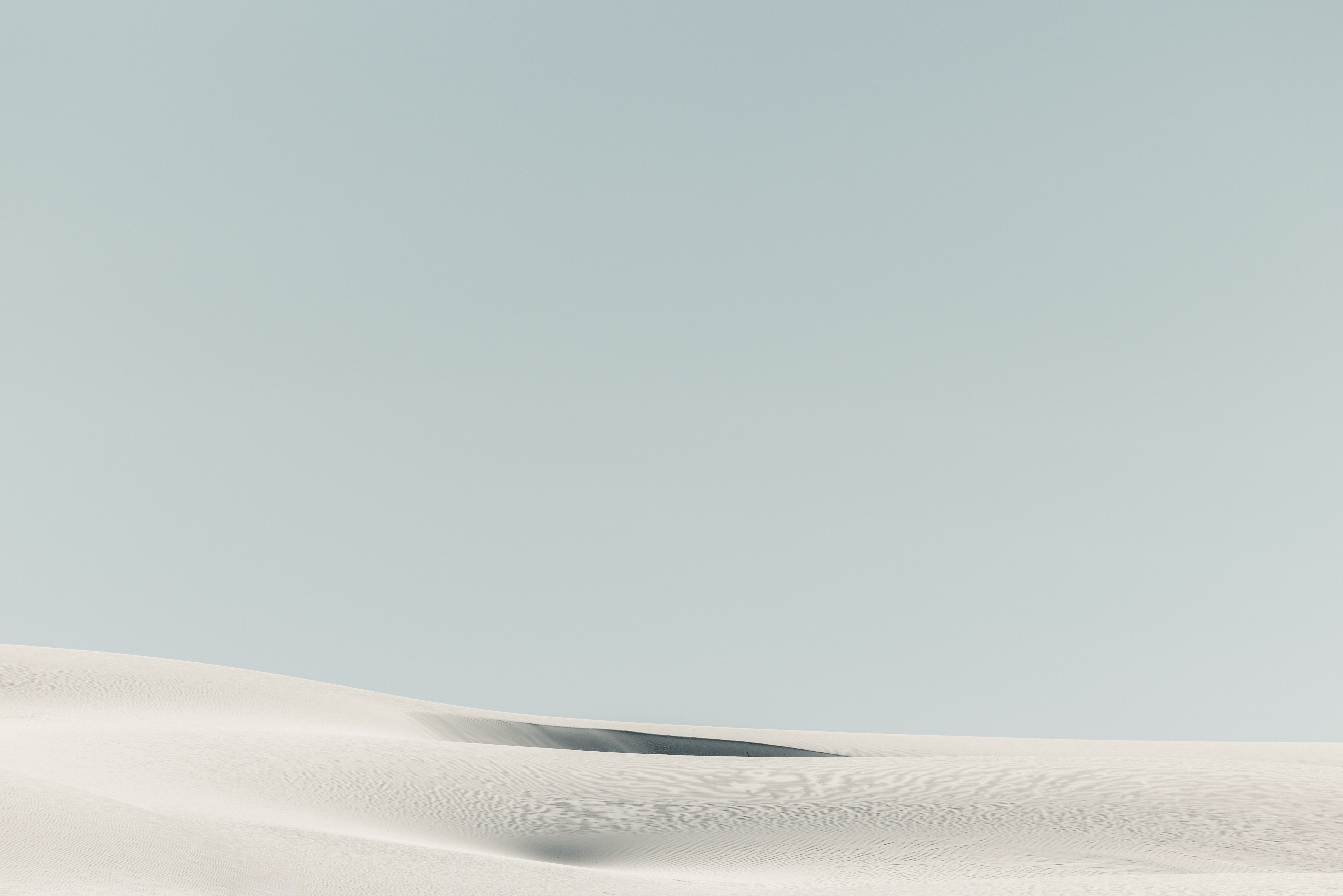 Soft white sand dunes under a pale blue sky