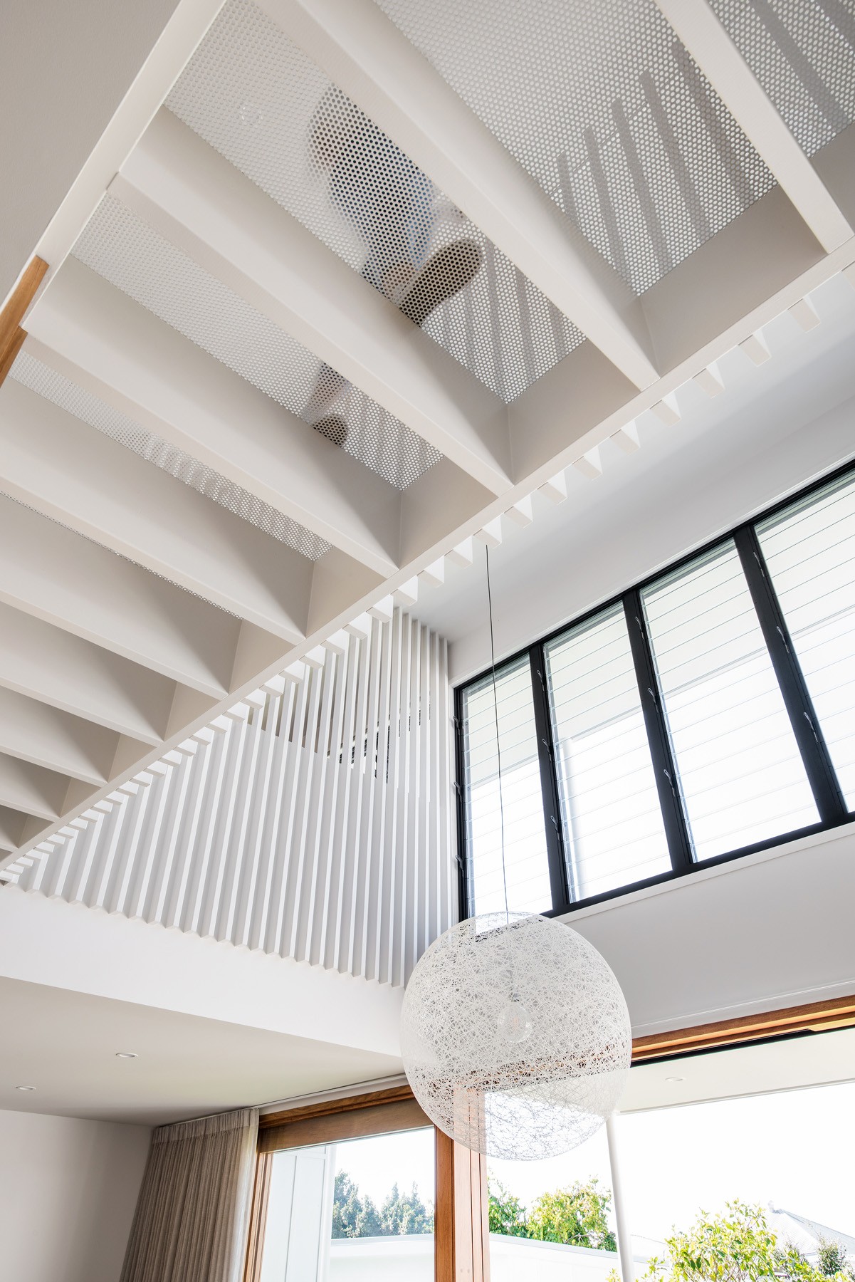Double-height interior of Ridge House with exposed ceiling structure, batten screening, and high-level glazing drawing daylight deep into the home.