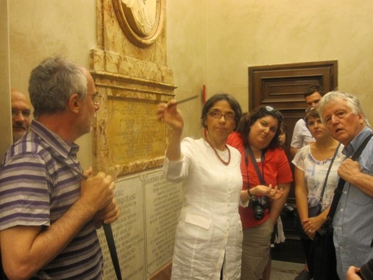 A photo of a group of students following a lecture while sitting near some text engraved wall.