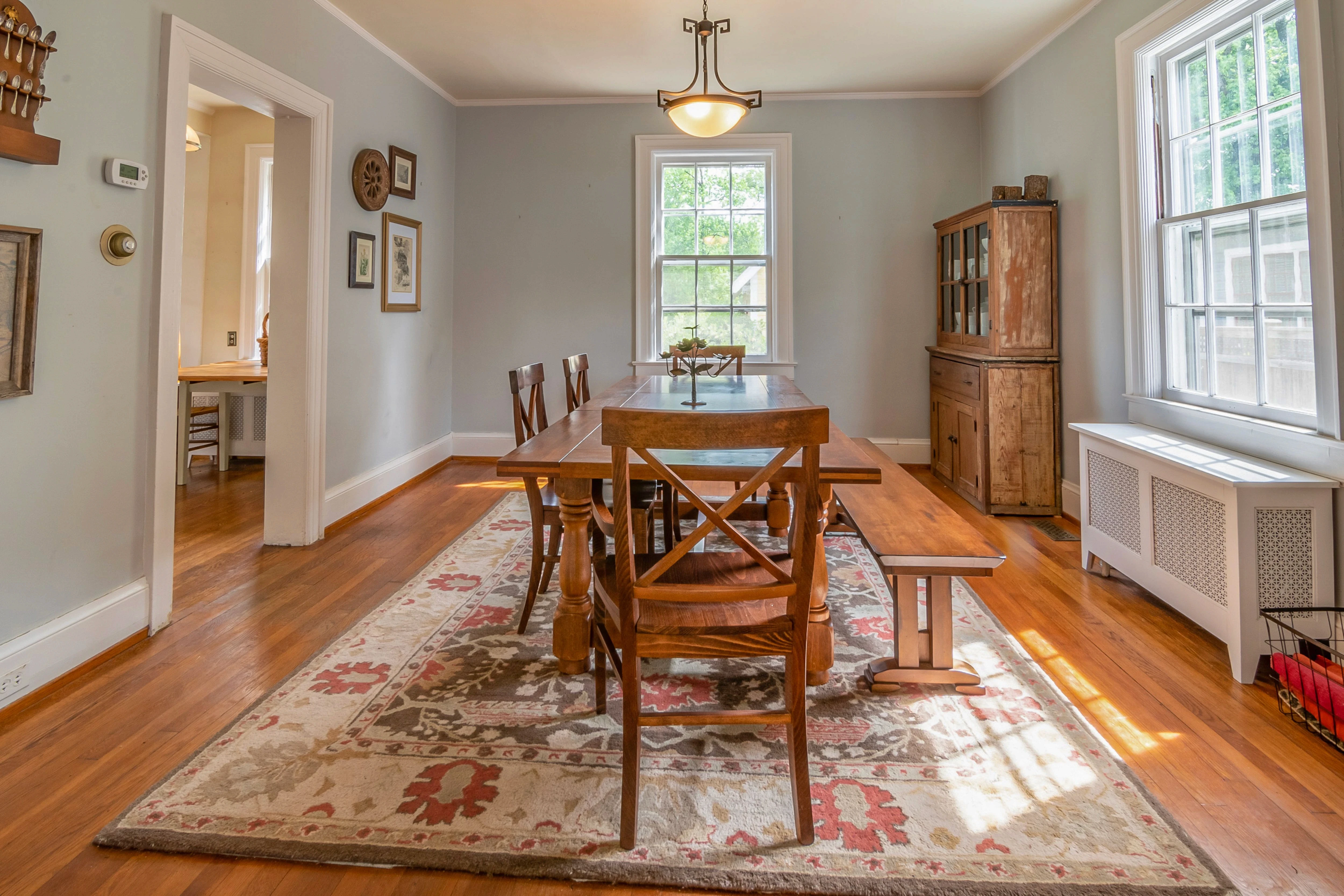 Rustic dining room with wooden table, chairs, patterned rug, and bright natural light.
