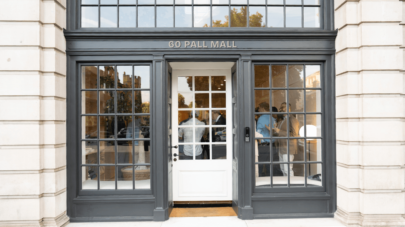 C-Suite-Invitationer and a woman in a light sweater sit at a desk with a laptop, discussing something. The room is dimly lit, creating a focused atmosphere.