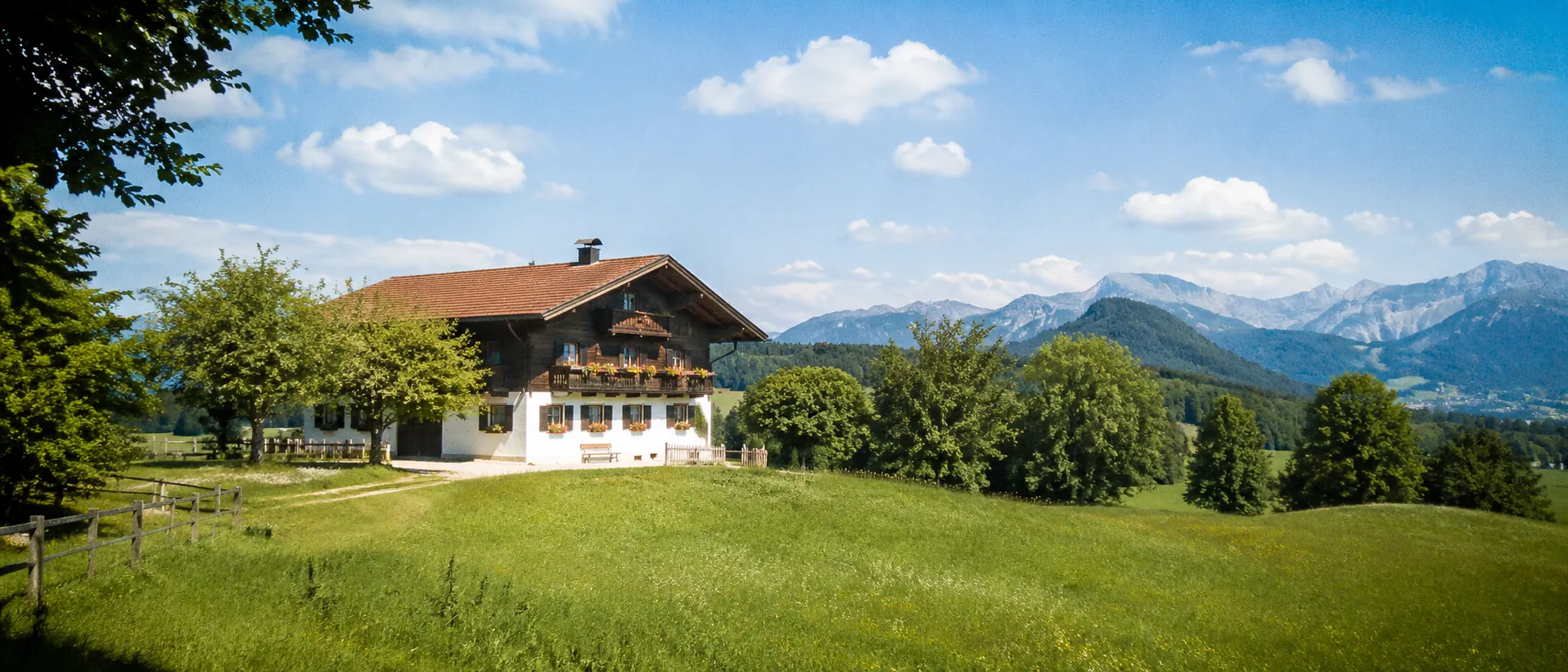 Helle bayerische Landschaft mit Bauernhaus, grünen Wiesen und Alpen im Hintergrund