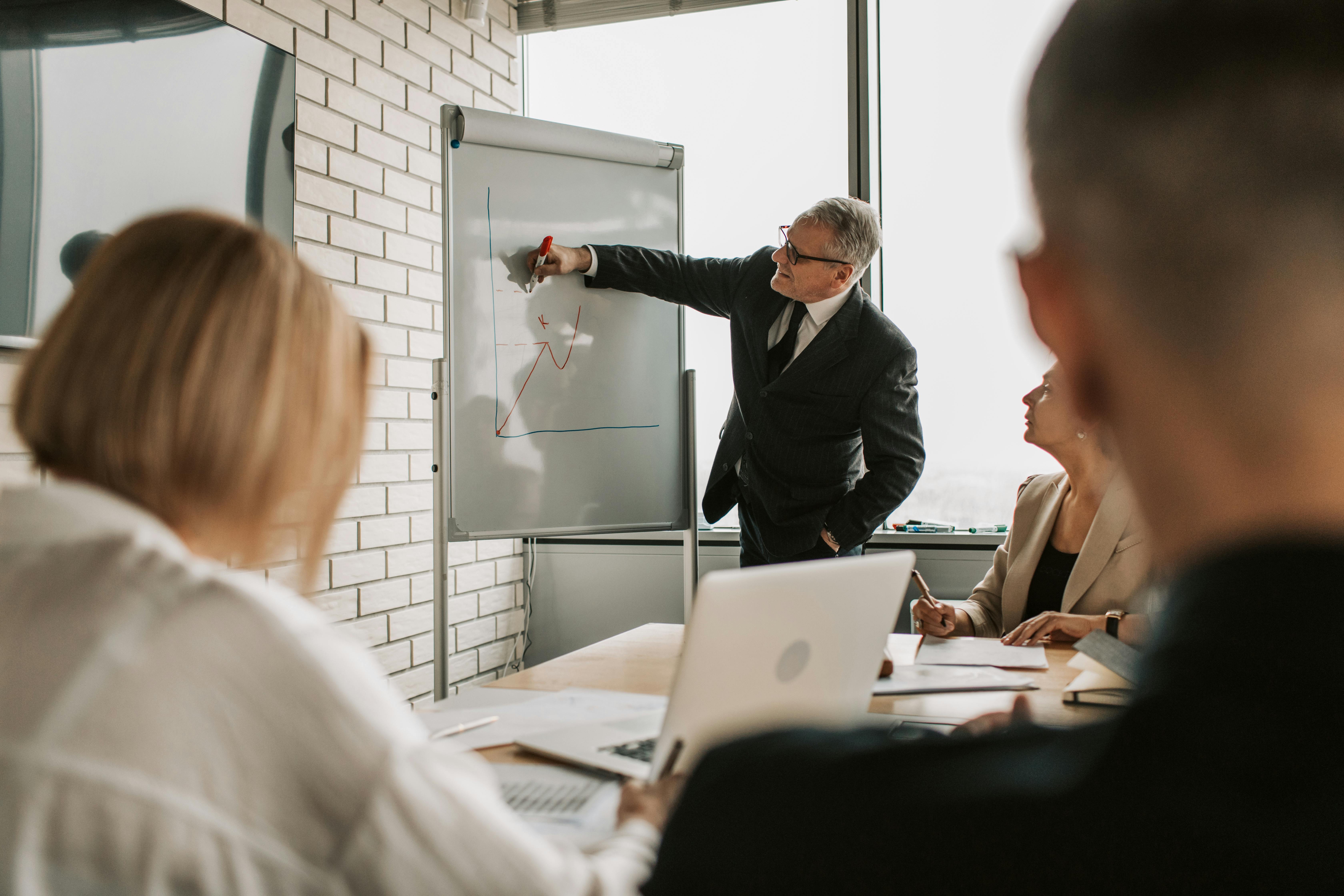 a-focused-business-team-engaging-in-a-meeting-with-a-presentation-on-a-whiteboar - vlada-karpovich (pexels)