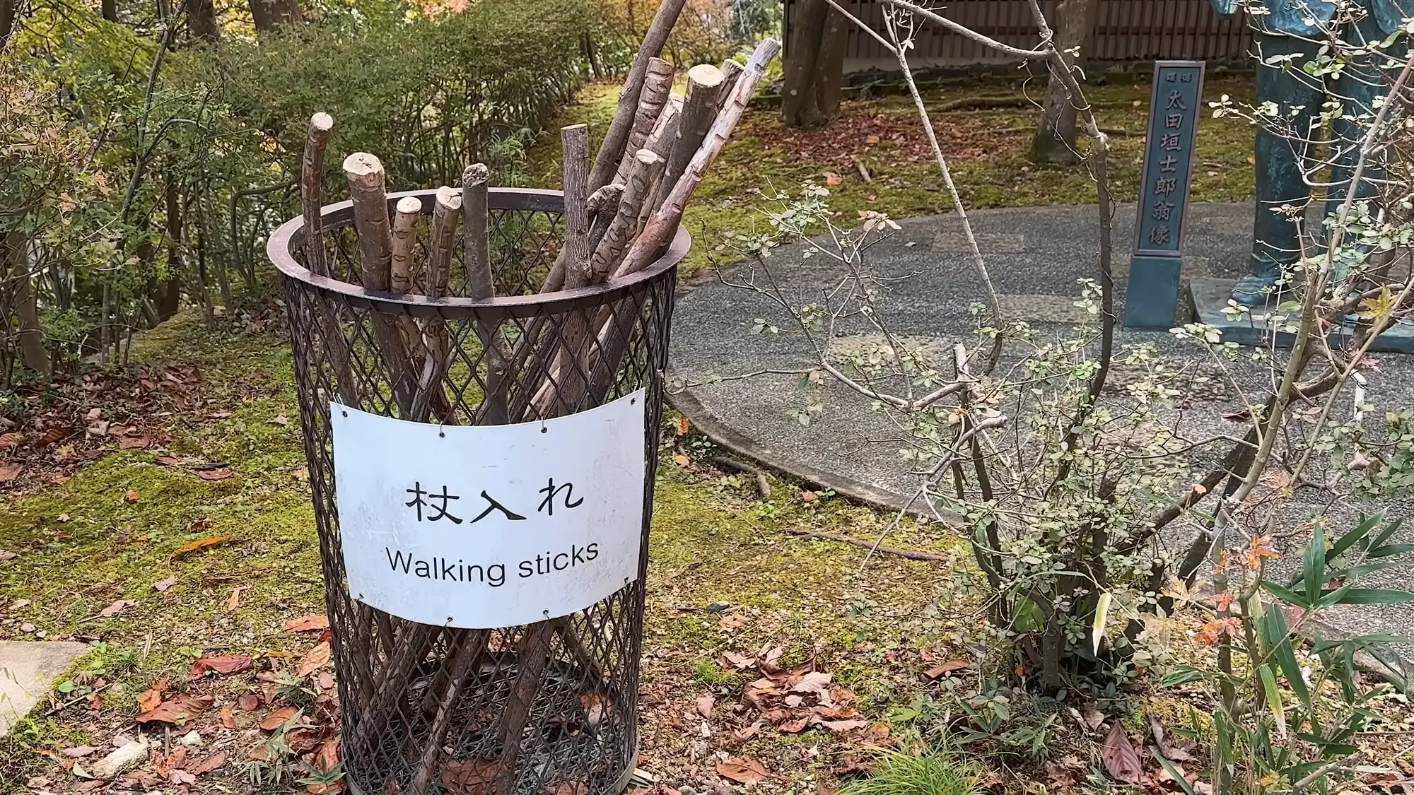 A metal basket of lending walking sticks under a sign reading Walking sticks at Onsenji, Kinosaki.