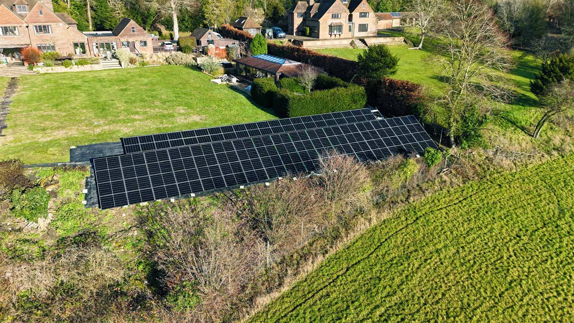 Large ground-mounted solar array installed on a south-facing hillside at Touchwood House, Puttenham, powering a countryside home and swimming pool.