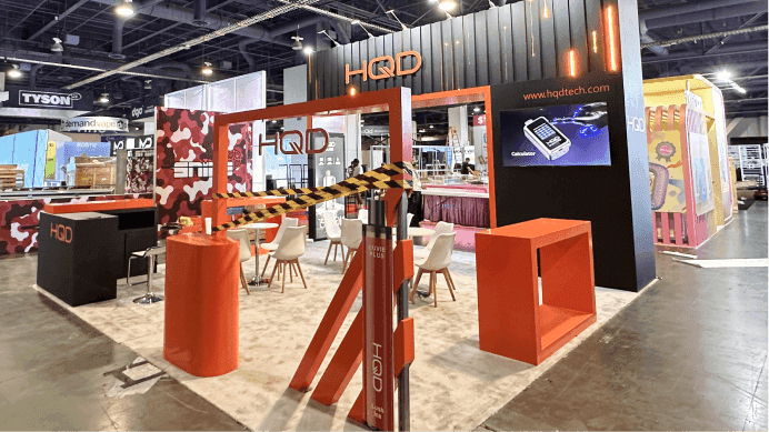 HQD CHAMPS Las Vegas 2025 July 20x20 booth front overview with branded facade, open meeting area, and retail product display