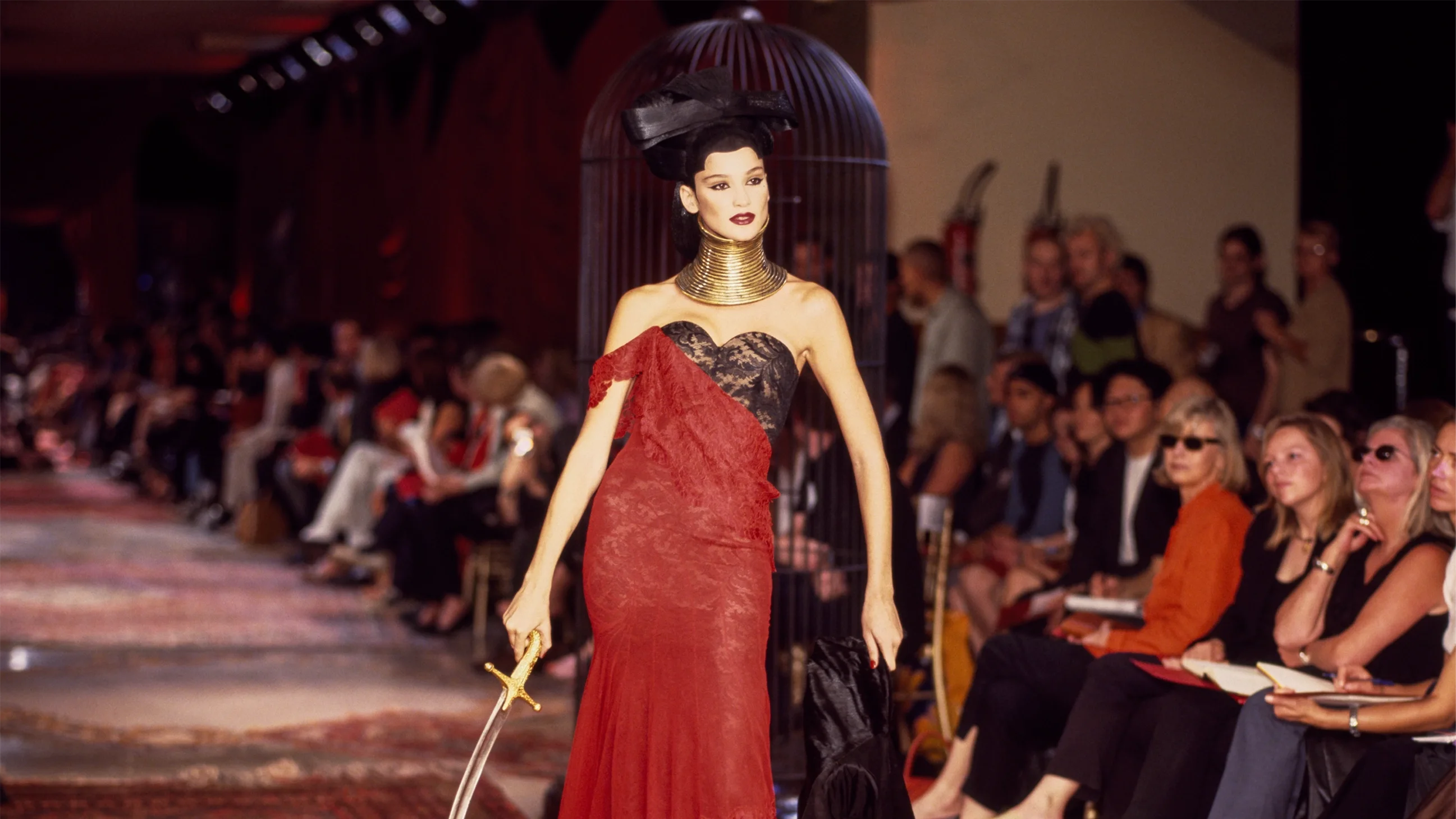 Runway model wearing a tall, structured gold coiled neckpiece designed by Shaun Leane for Givenchy haute couture by Alexander McQueen, styled with a red lace gown.