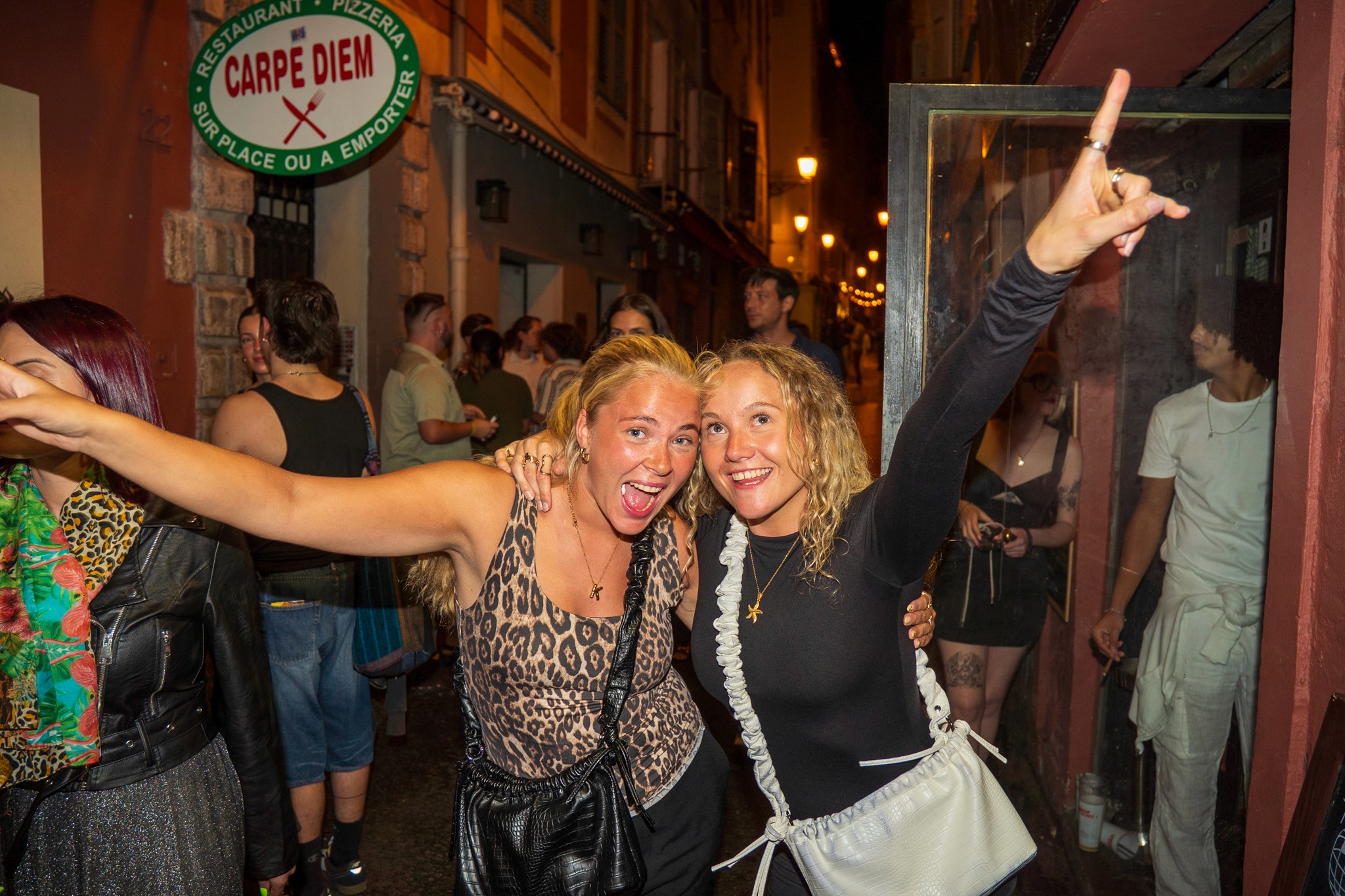 A weekend nightlife scene in Nice with friends heading out near the Old Town, dressed casually, carrying small bags under warm street lights.