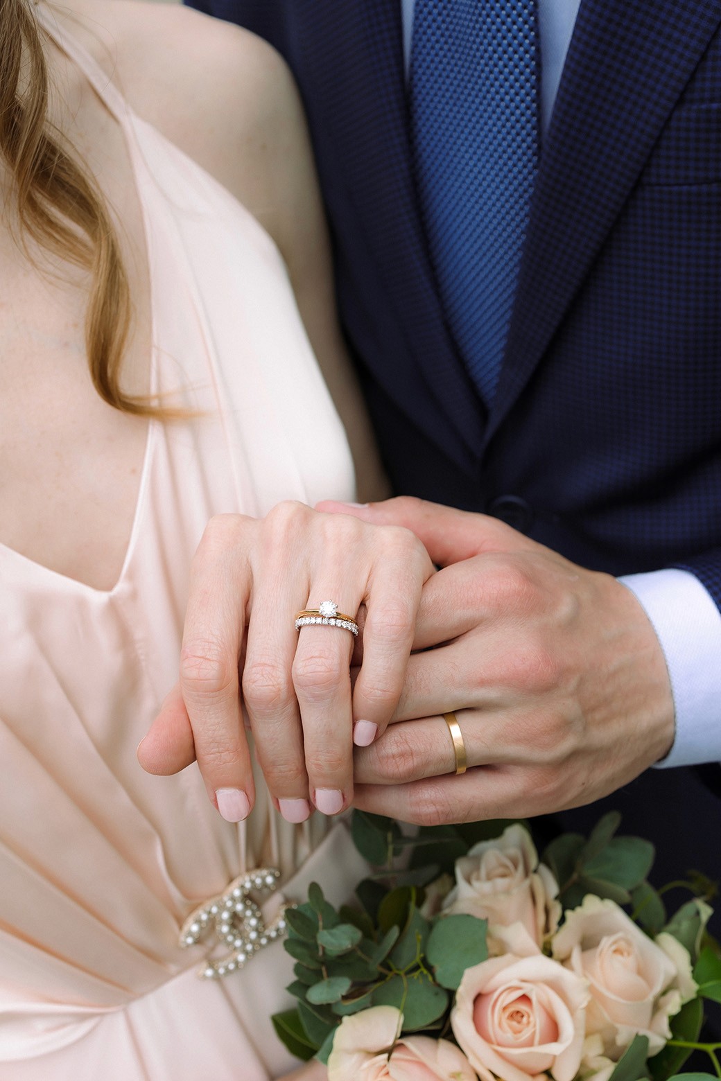Elegant close-up wedding portrait featuring bridal rings, bouquet details and tailored blue suit styling