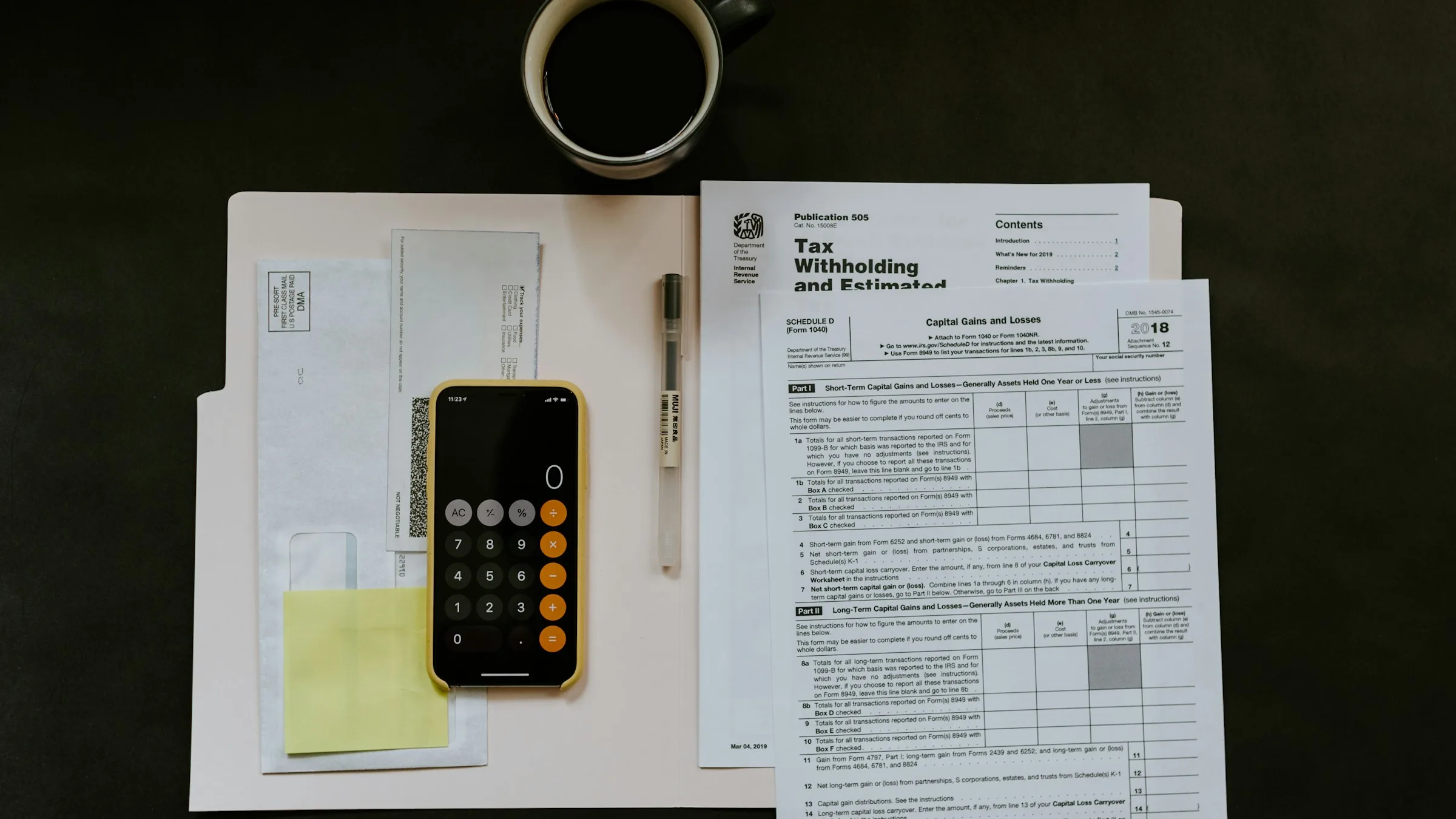 Federal tax forms, a calculator on a phone and a coffee cup on a desk, ready for preparing a tax return