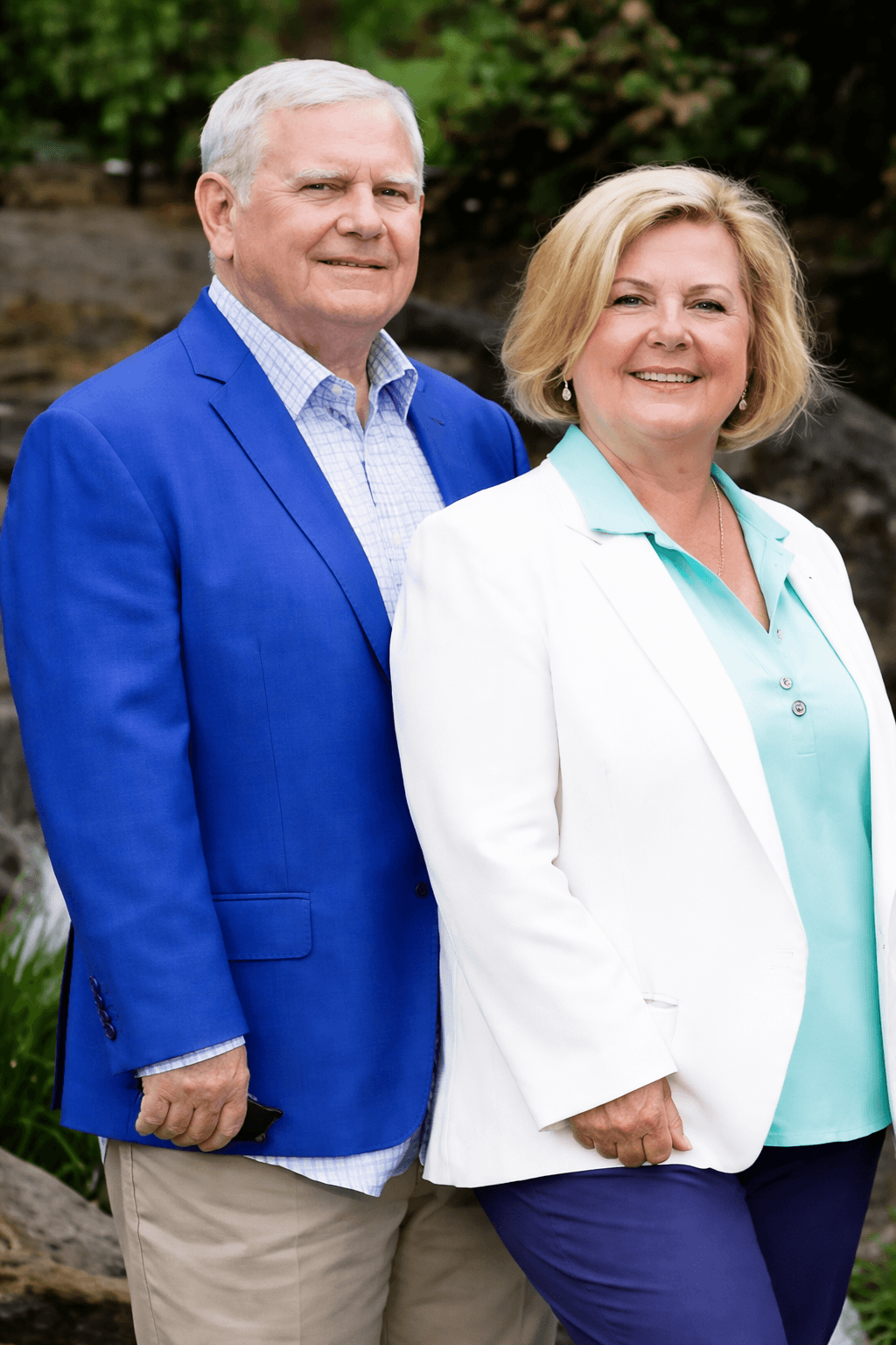 A serene outdoor seating area with two chairs, surrounded by lush greenery and a glassed-in structure.