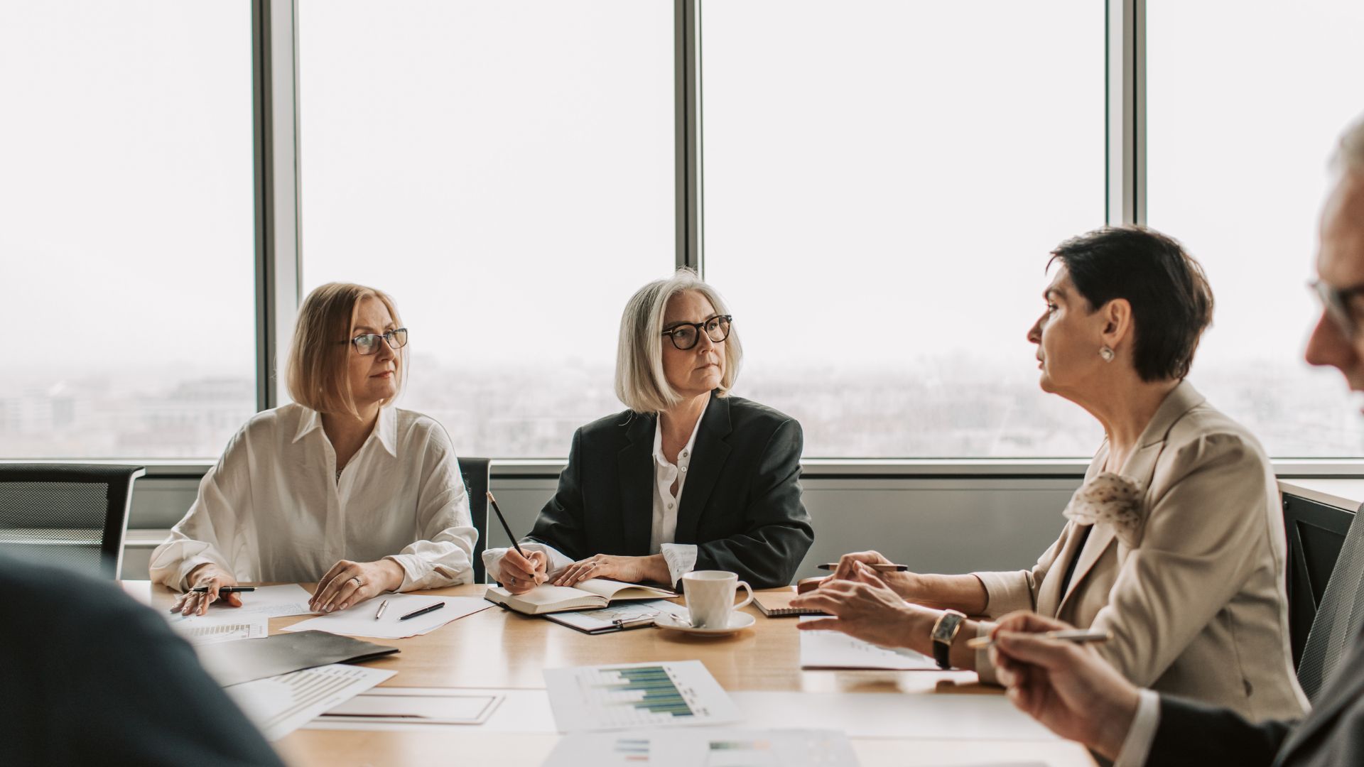 Senior leaders in serious discussion at a boardroom table by a window