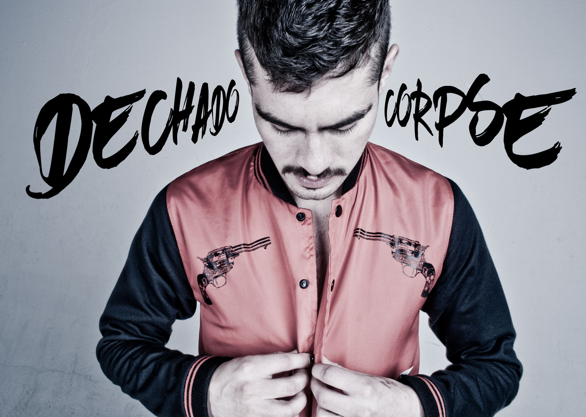 Frontal view of a man looking down while buttoning a red and black bomber jacket featuring two revolver illustrations on the chest. Large "DECHADO CORPSE" text is overlaid in the background.